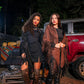 Two women standing in front of a truck with pumpkins at night.