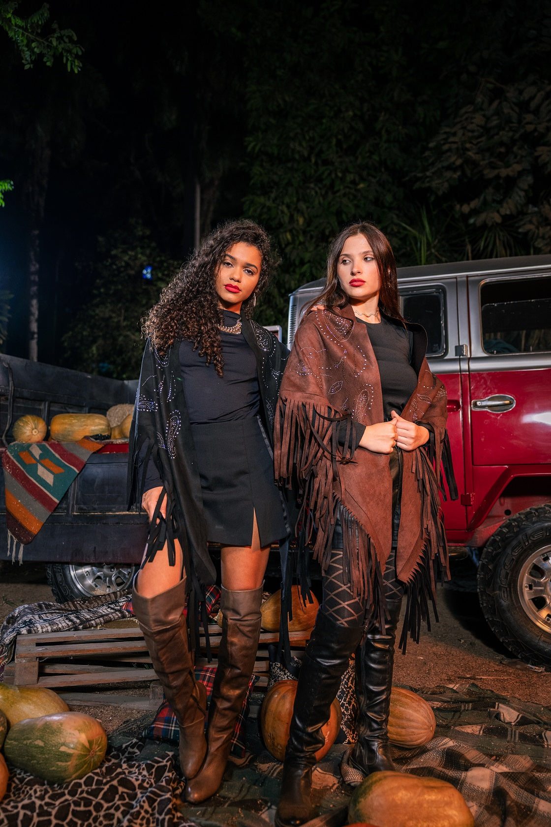 Two women standing in front of a truck with pumpkins at night.
