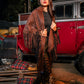 Woman in a brown poncho standing in front of a red truck with pumpkins and autumn decorations.