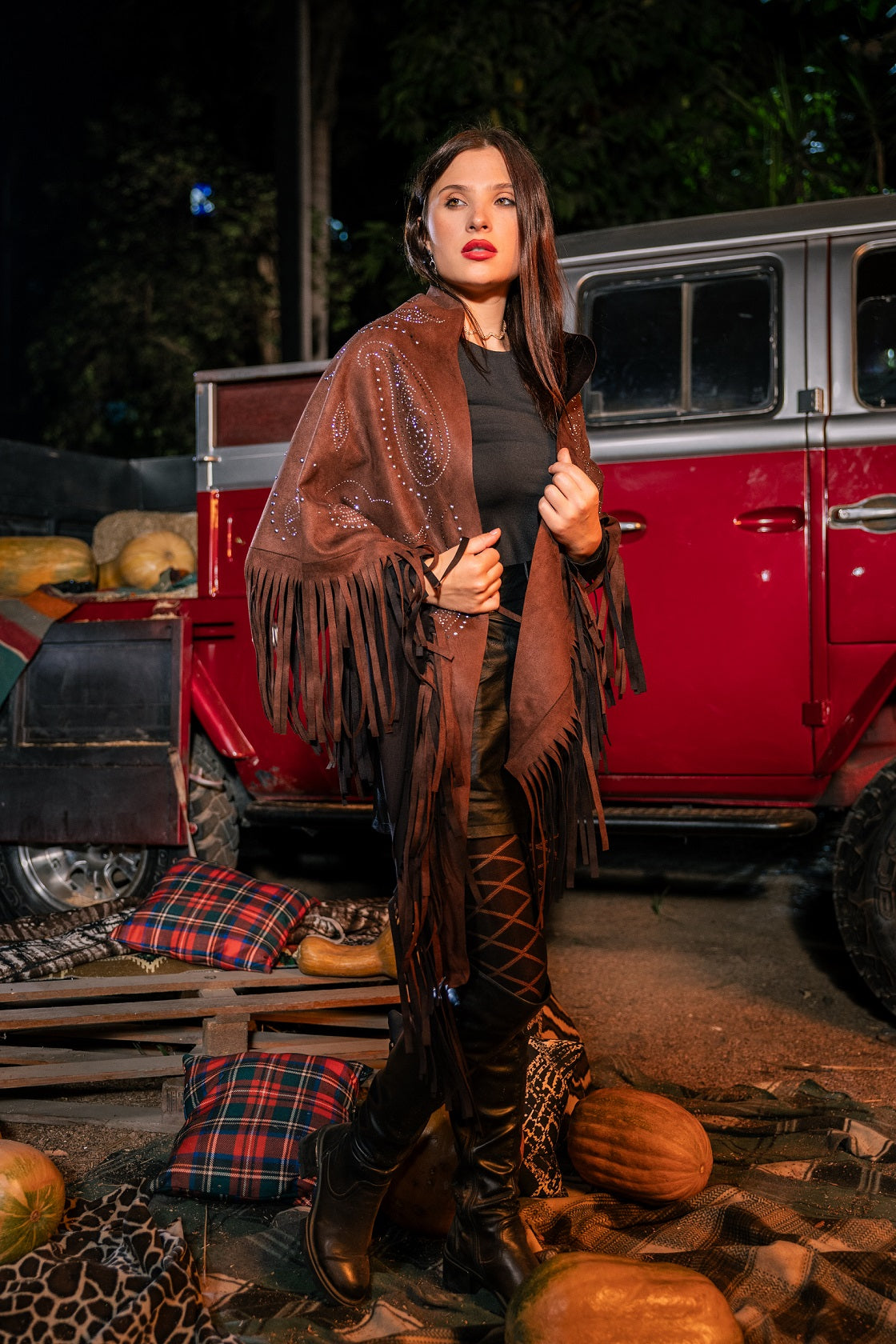Woman in a brown poncho standing in front of a red truck with pumpkins and autumn decorations.