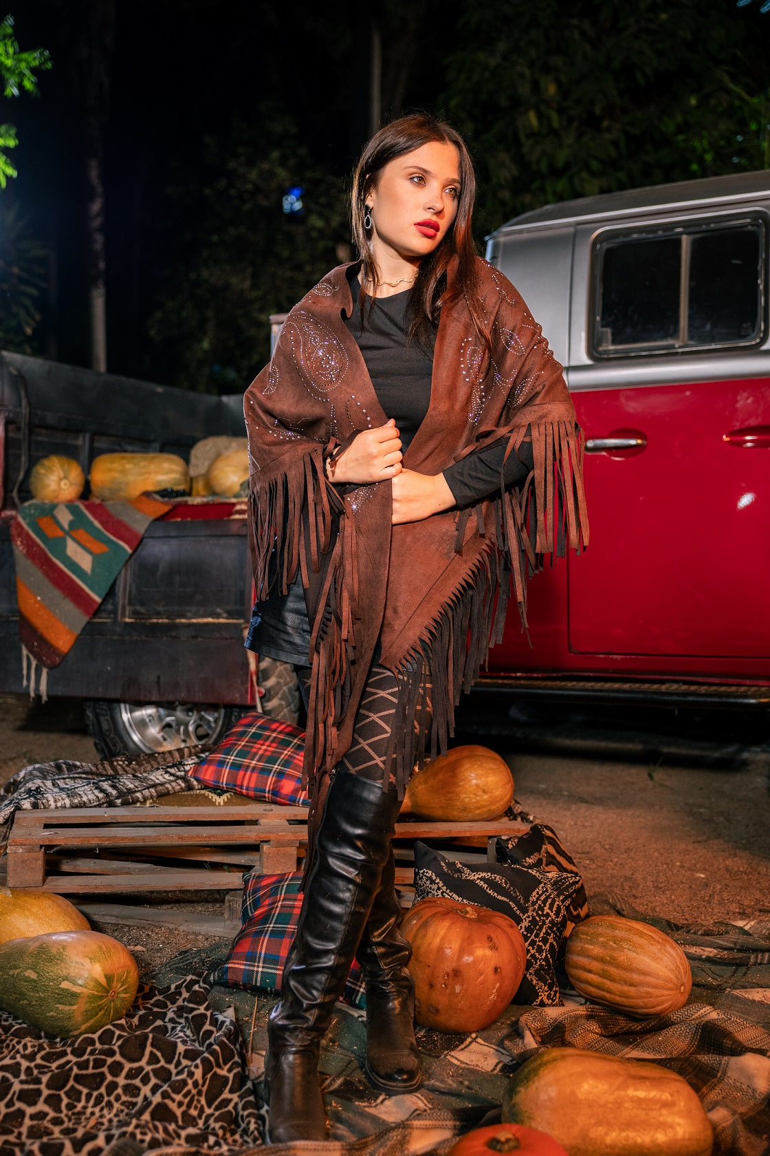 Woman in a brown fringed poncho standing in front of a red truck with pumpkins around.
