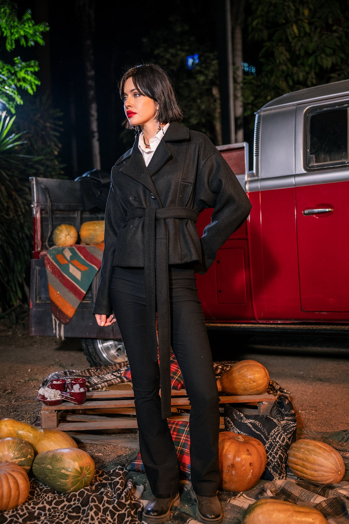 Woman standing in front of a vintage car with pumpkins at night