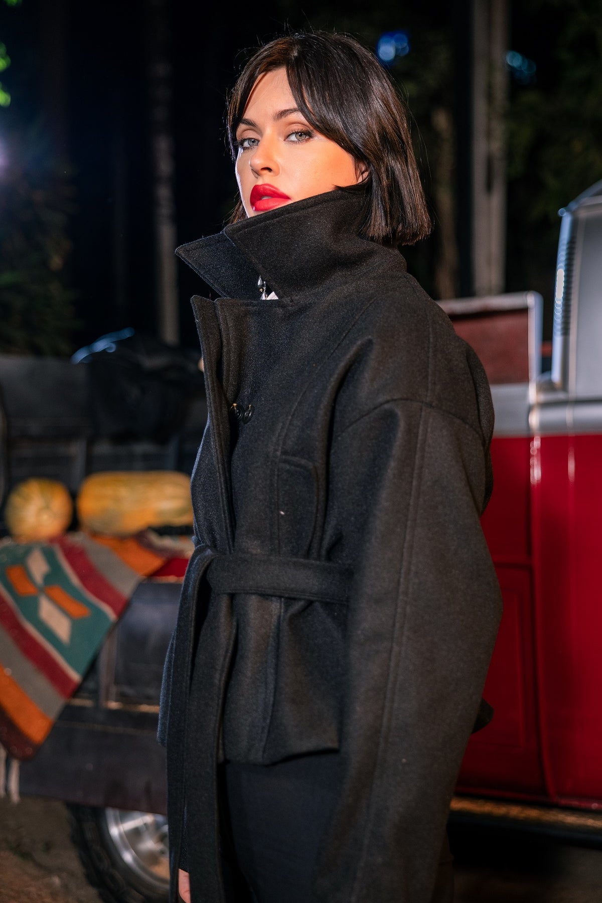 Woman wearing a black coat standing in front of a red vehicle with a colorful blanket.