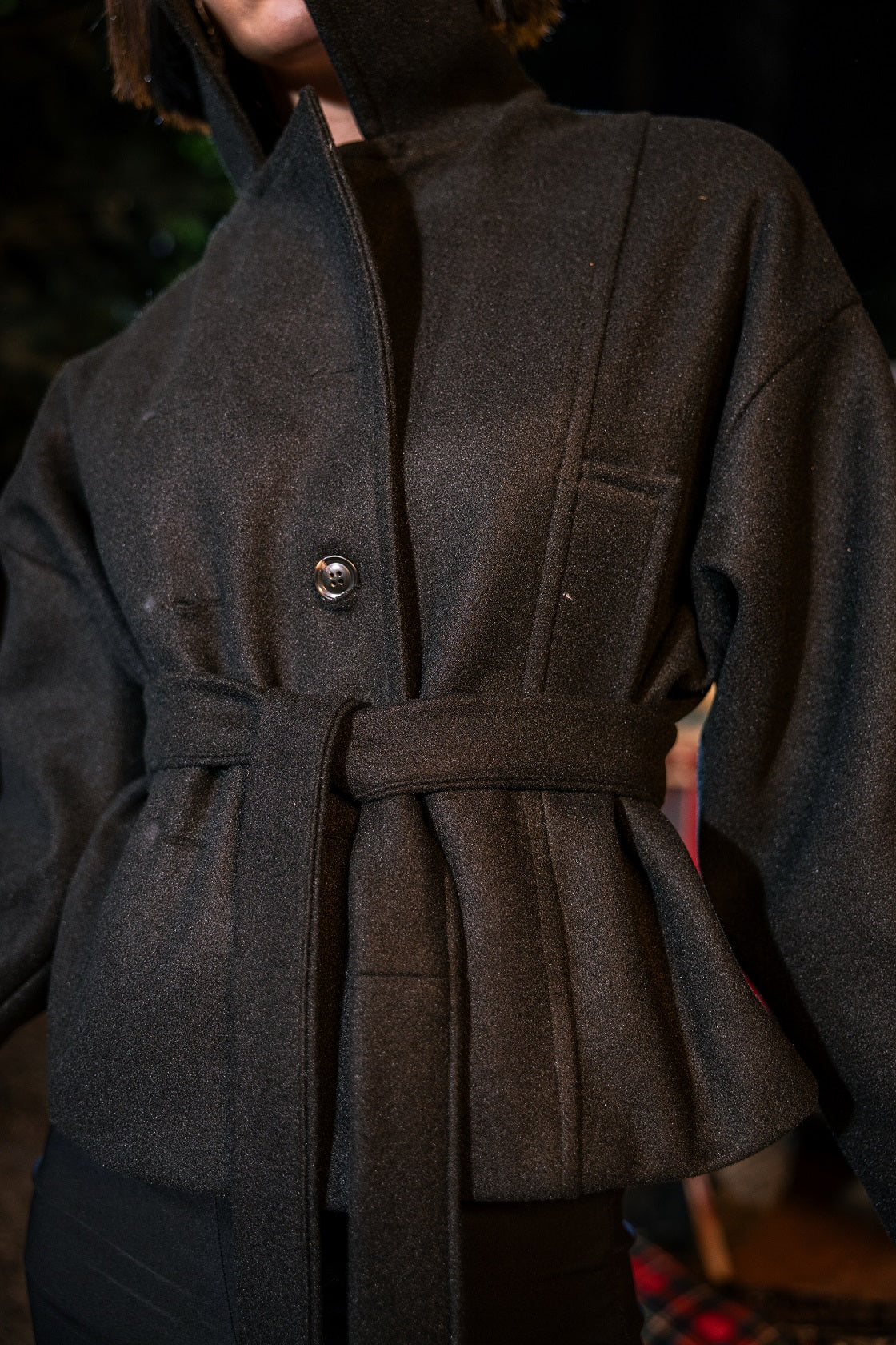 Dark brown coat with a belt worn by a person, blurred background