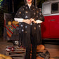 Woman wearing a black star-patterned poncho standing in front of a vintage car with pumpkins around.