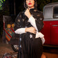 Woman wearing a black patterned scarf in an outdoor setting with a red vehicle and pumpkins.
