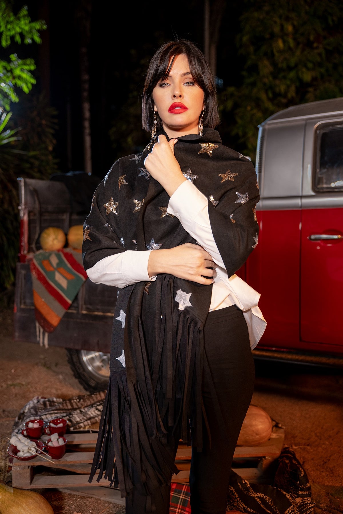 Woman wearing a black patterned scarf in an outdoor setting with a red vehicle and pumpkins.