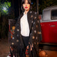 Woman wearing a black star-patterned shawl in front of a vintage red truck at night.
