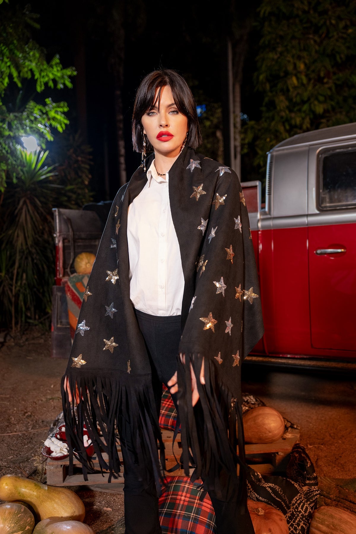 Woman wearing a black star-patterned shawl in front of a vintage red truck at night.