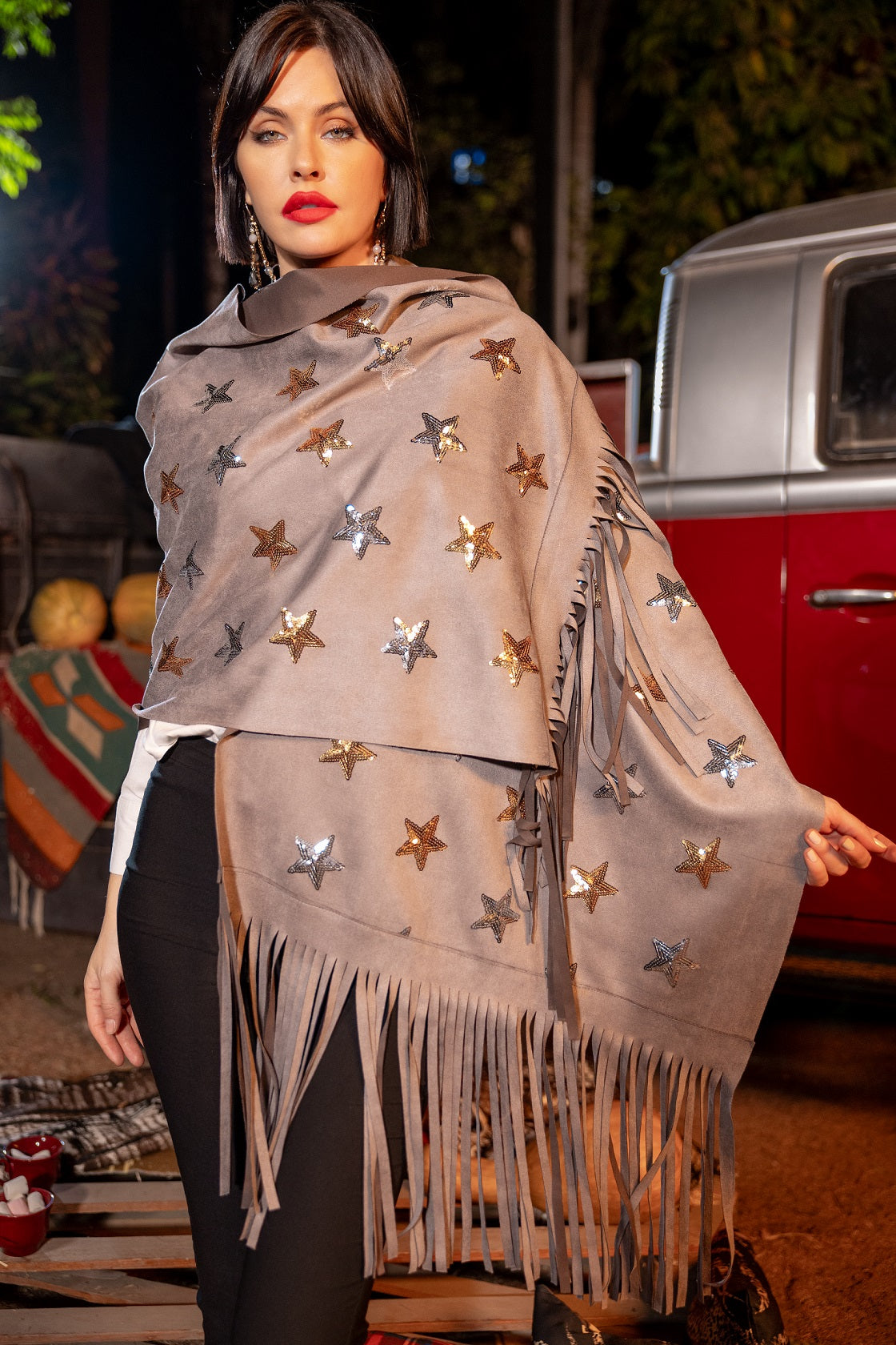 Woman wearing a star-patterned shawl with fringe in front of a vintage red truck.
