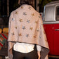 Person wearing a beige shawl with star patterns in front of a vintage red vehicle.