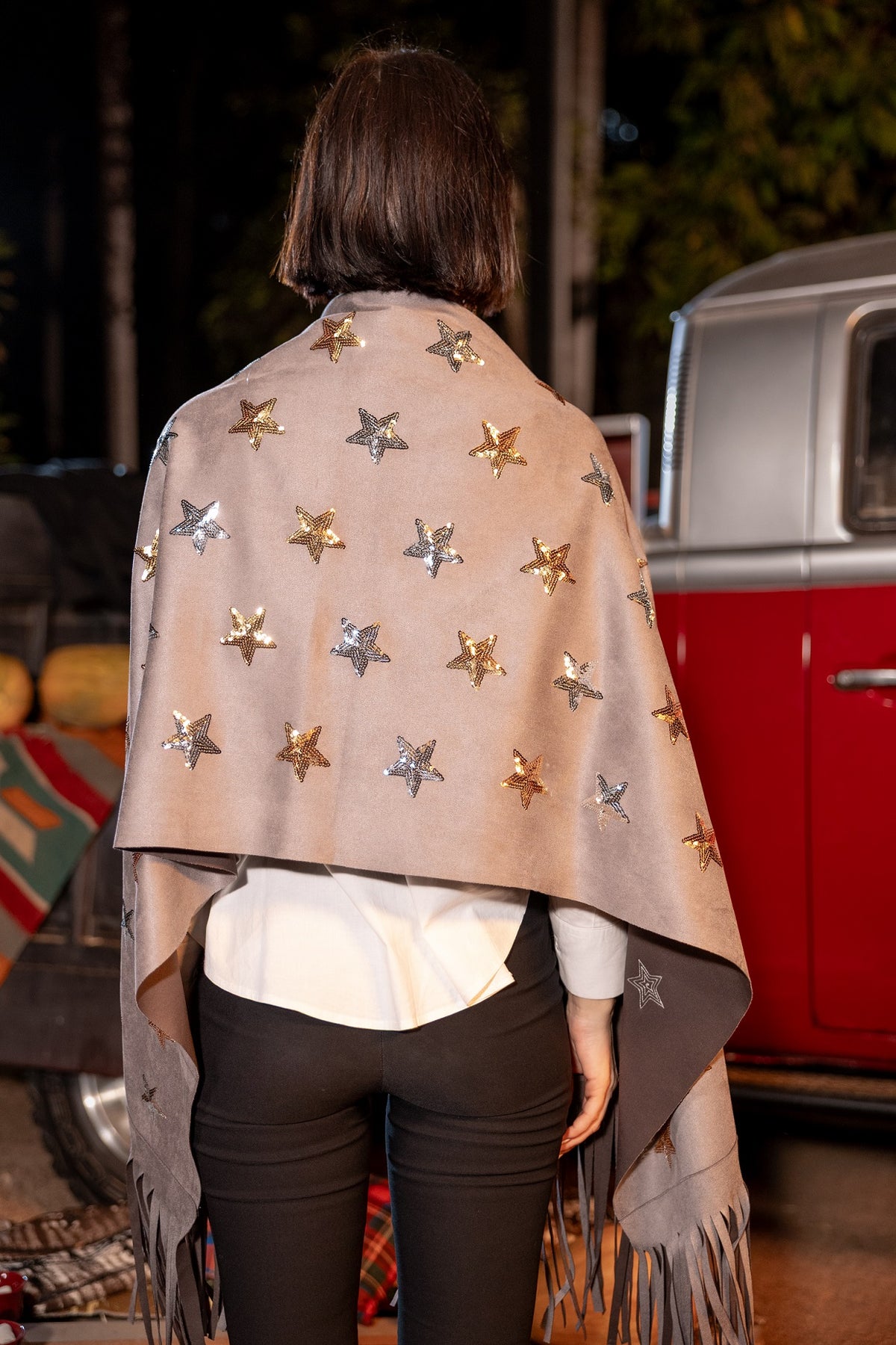 Person wearing a beige shawl with star patterns in front of a vintage red vehicle.
