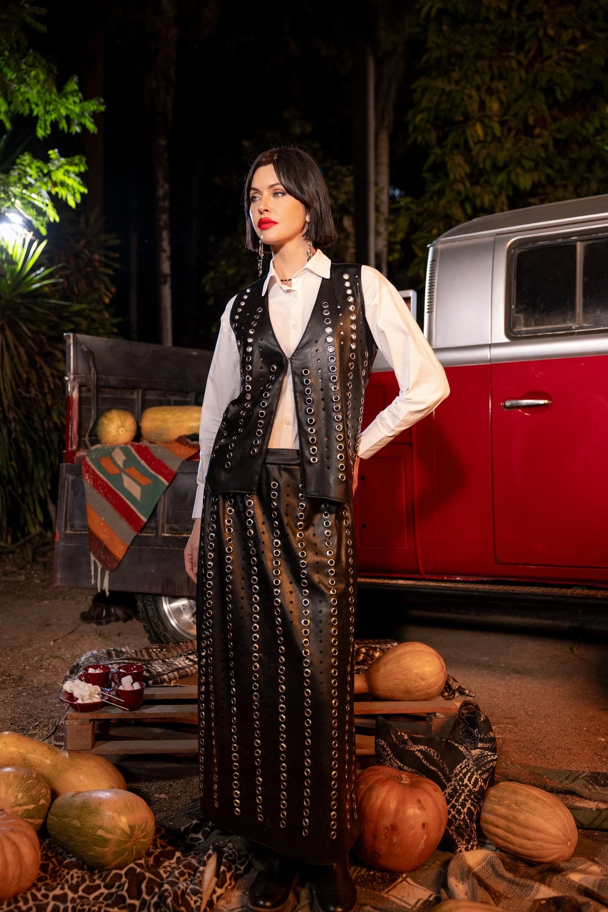 Woman in a stylish outfit standing in front of a vintage car with pumpkins around.