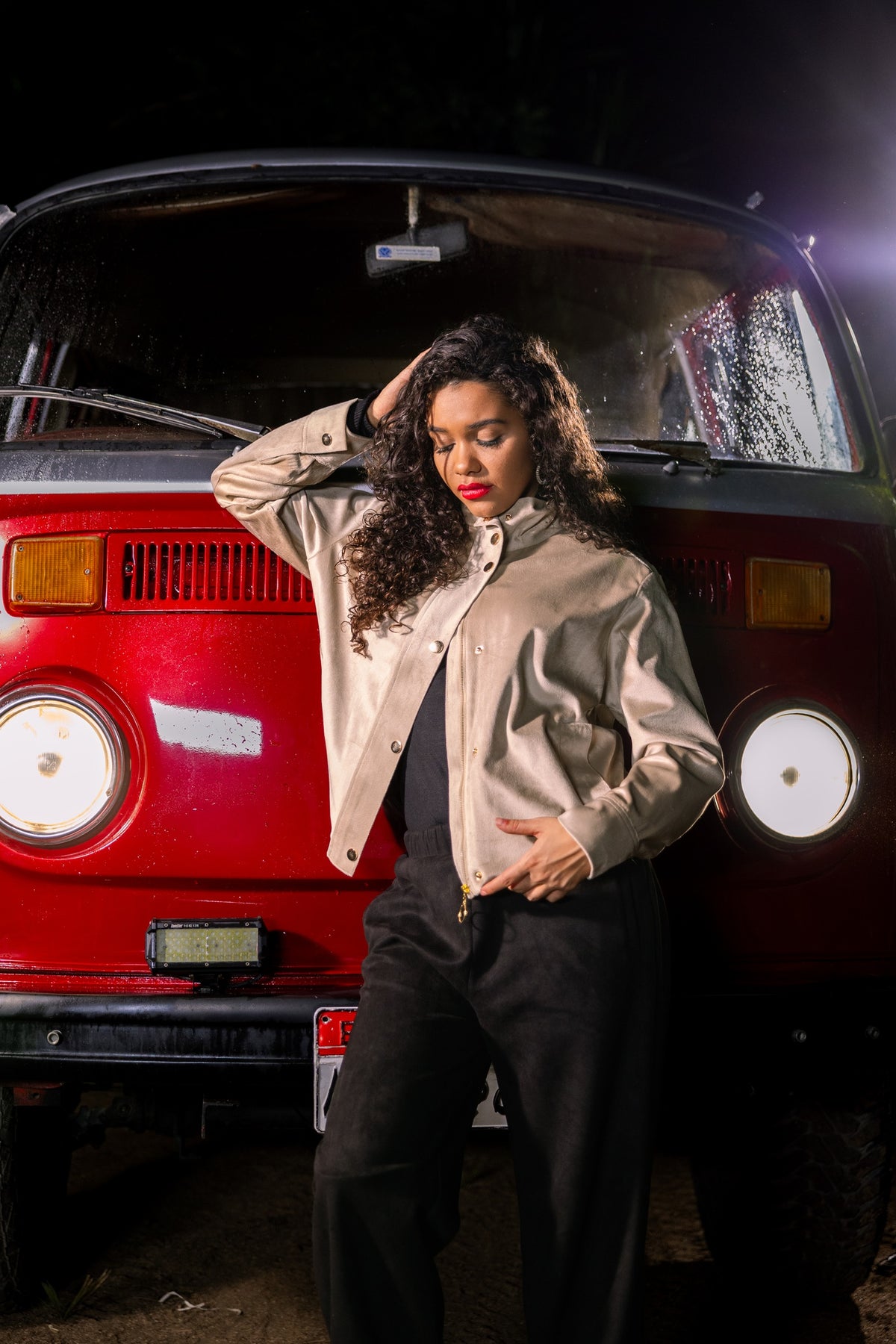 Woman posing in front of a red vintage van at night.