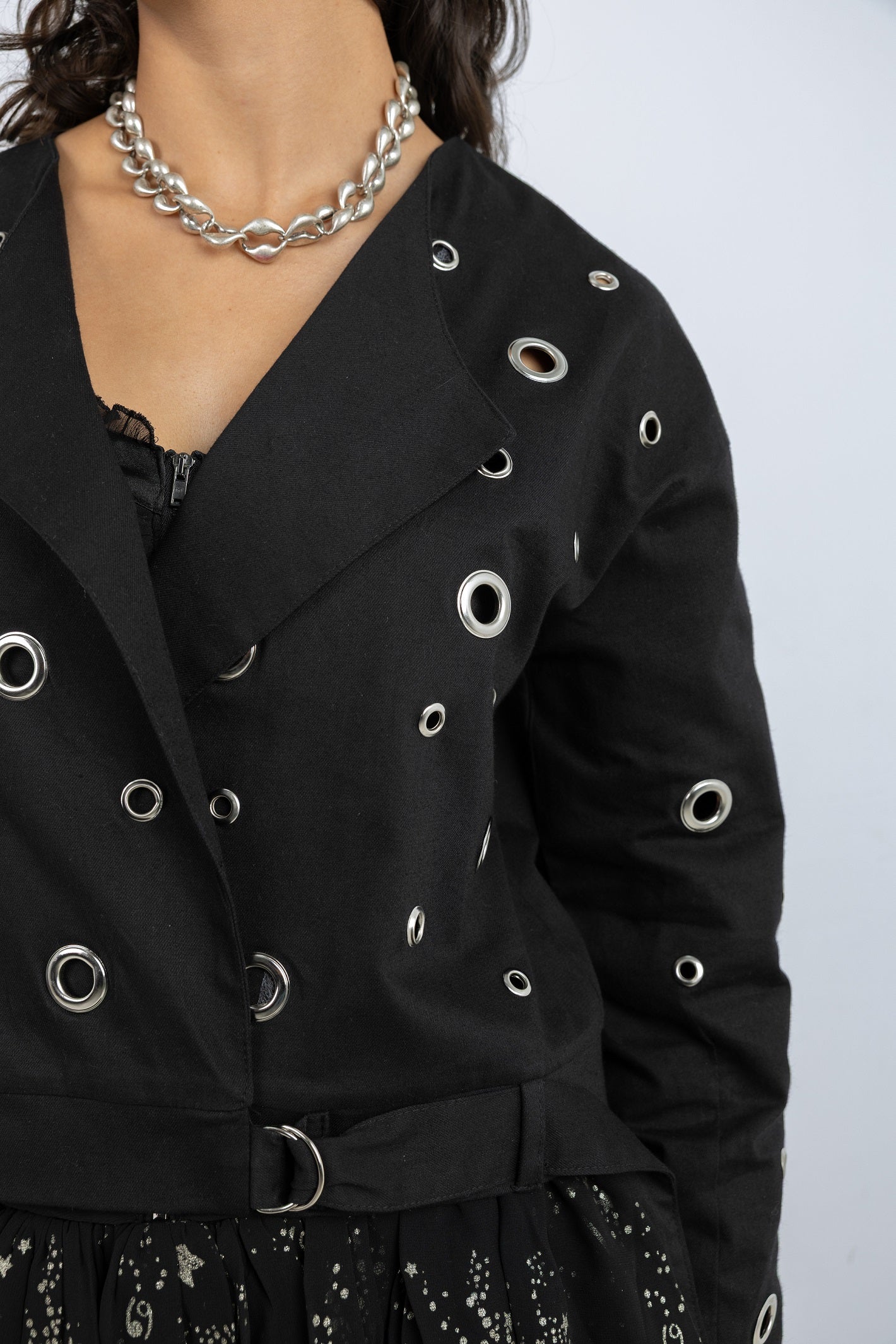 Black jacket with silver eyelet details on a plain background