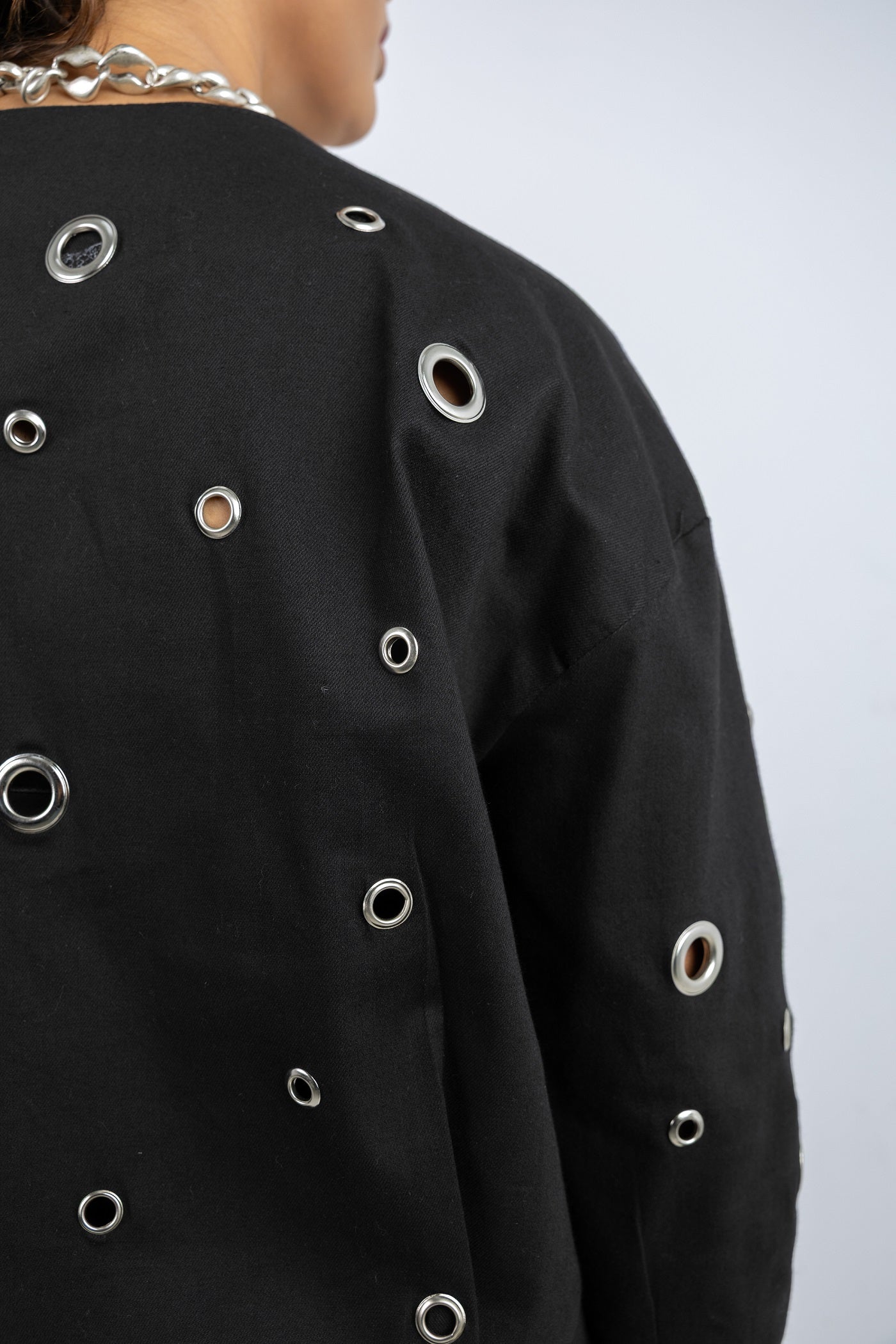 Black jacket with silver eyelet details on a plain background