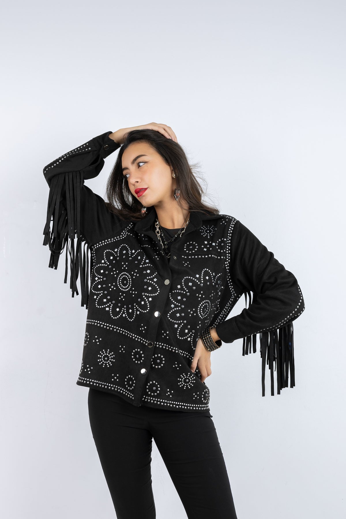 Woman wearing a black fringed jacket with intricate patterns on a white background