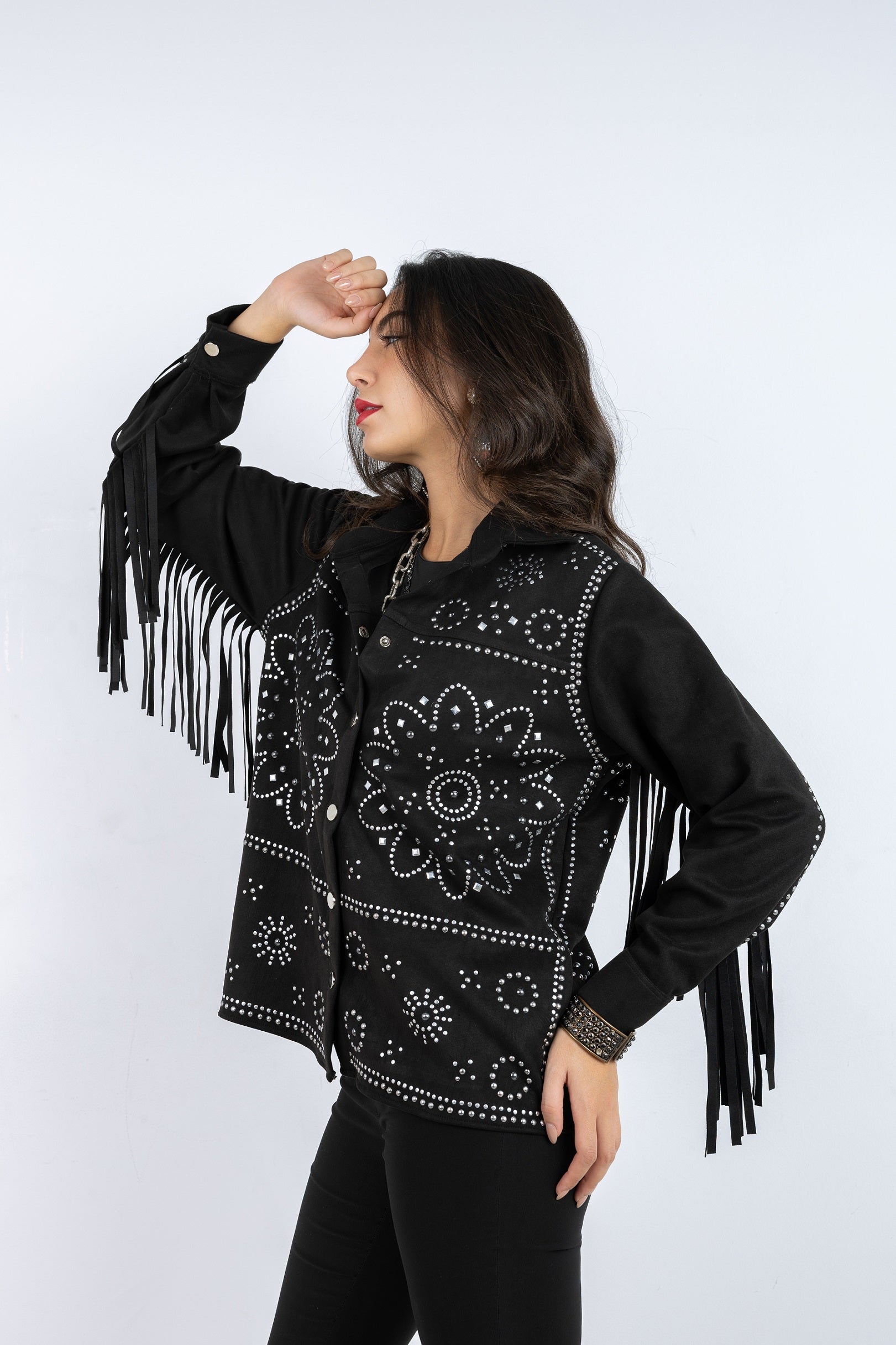Woman wearing a black jacket with fringe and intricate patterns on a white background
