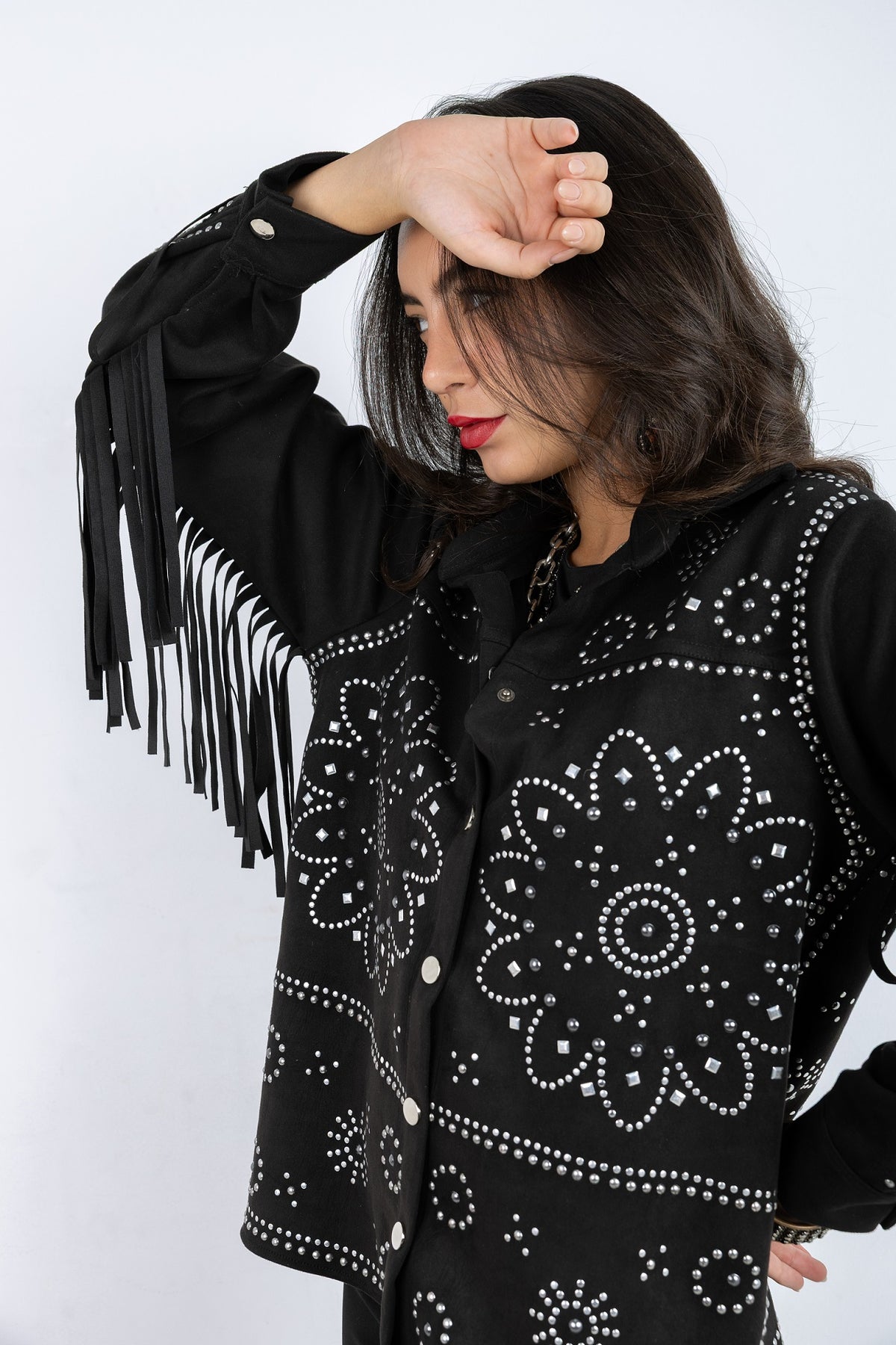 Woman wearing a black jacket with white patterns and fringes on a white background