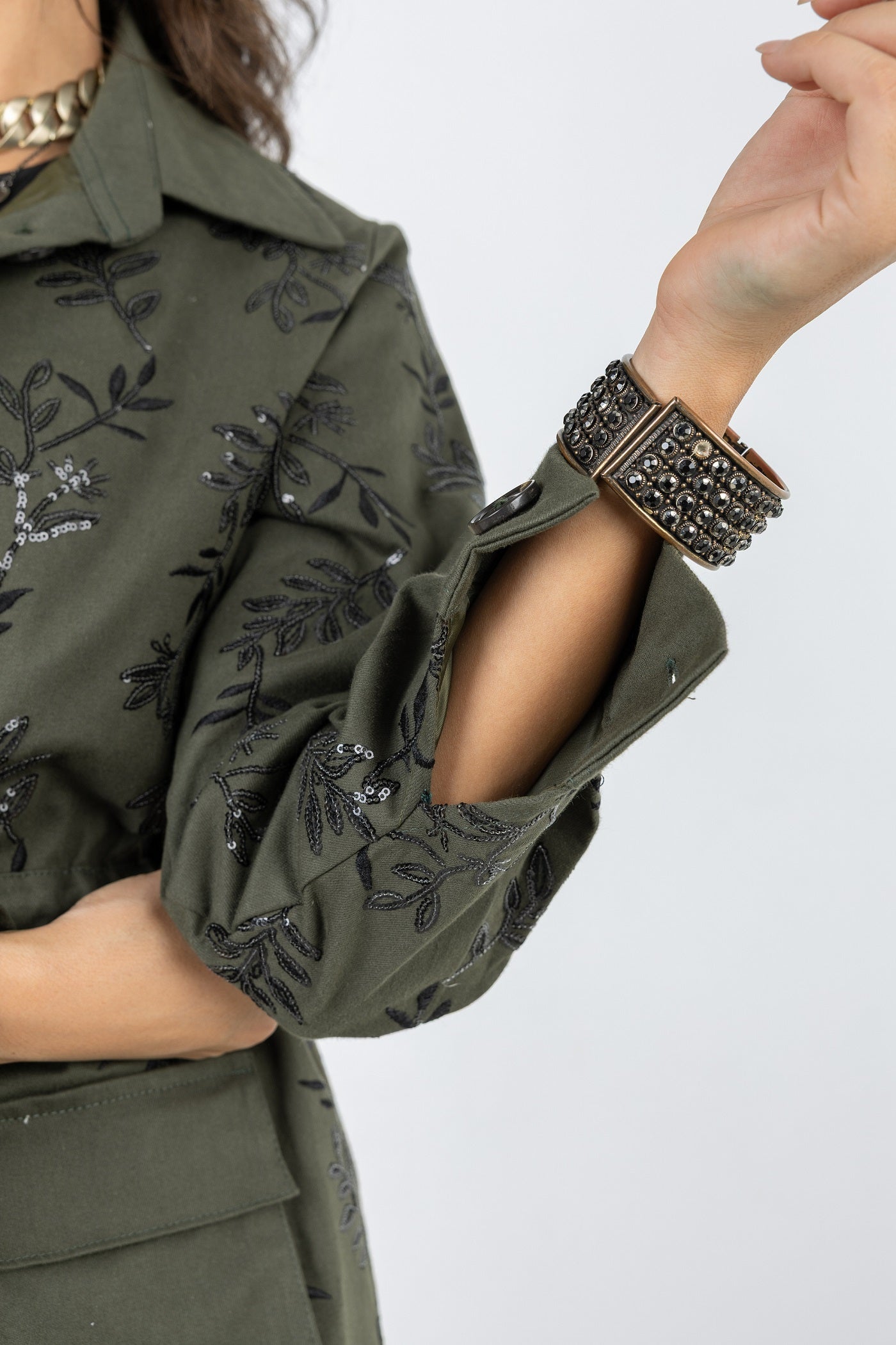 Person wearing an olive green shirt with black floral embroidery on a white background