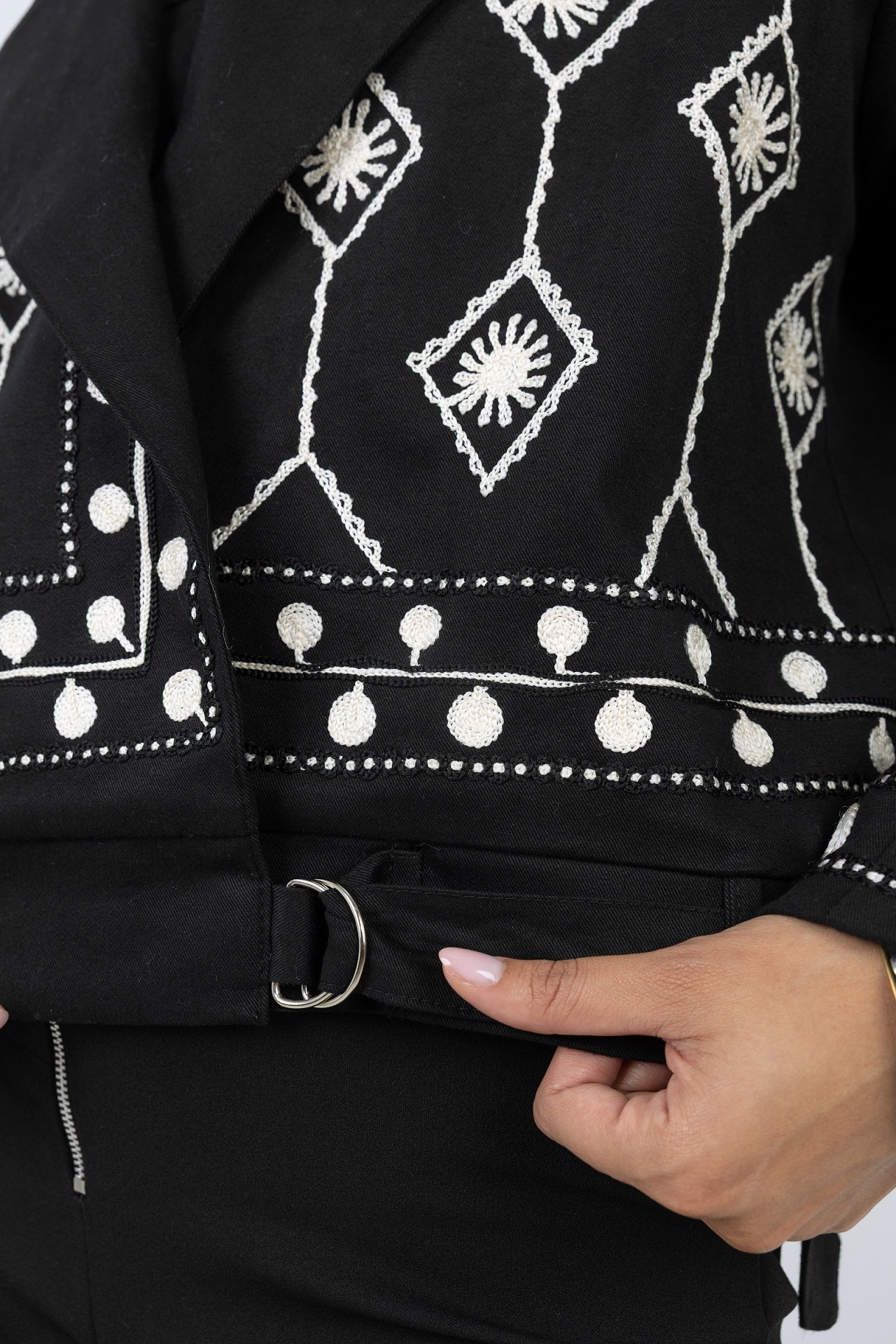 Black jacket with white embroidery and a hand adjusting the belt.