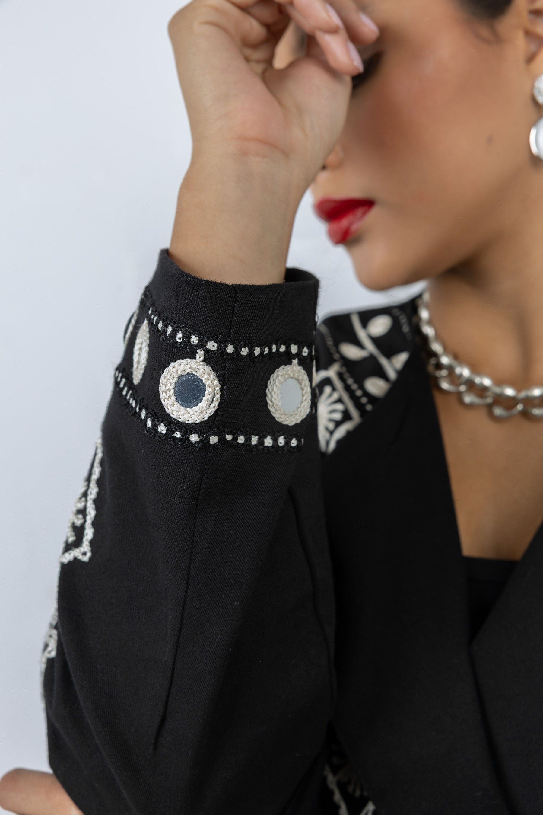 Close-up of a person wearing a black outfit with intricate white patterns and jewelry.