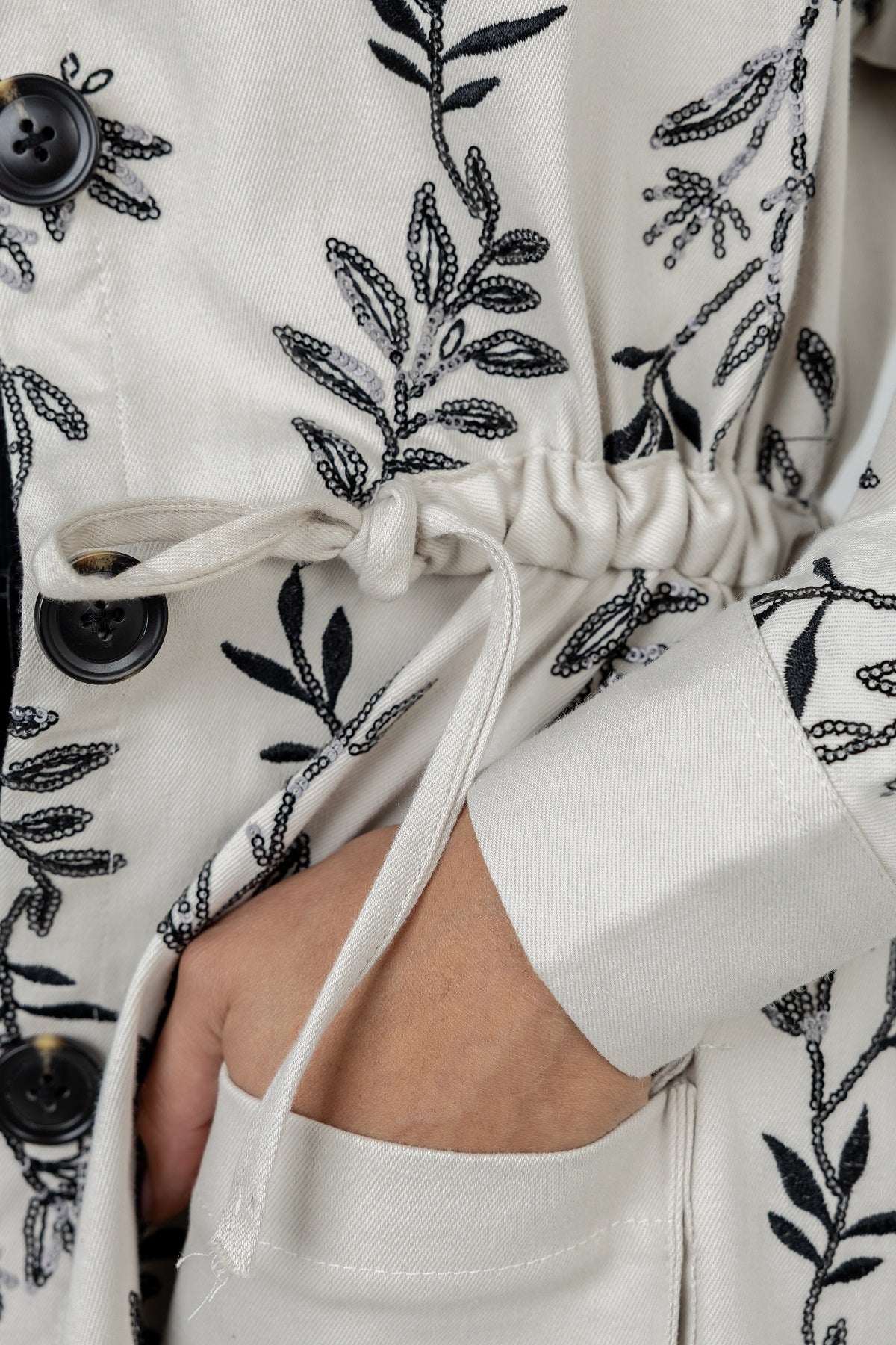 Close-up of a white garment with black floral embroidery and buttons.
