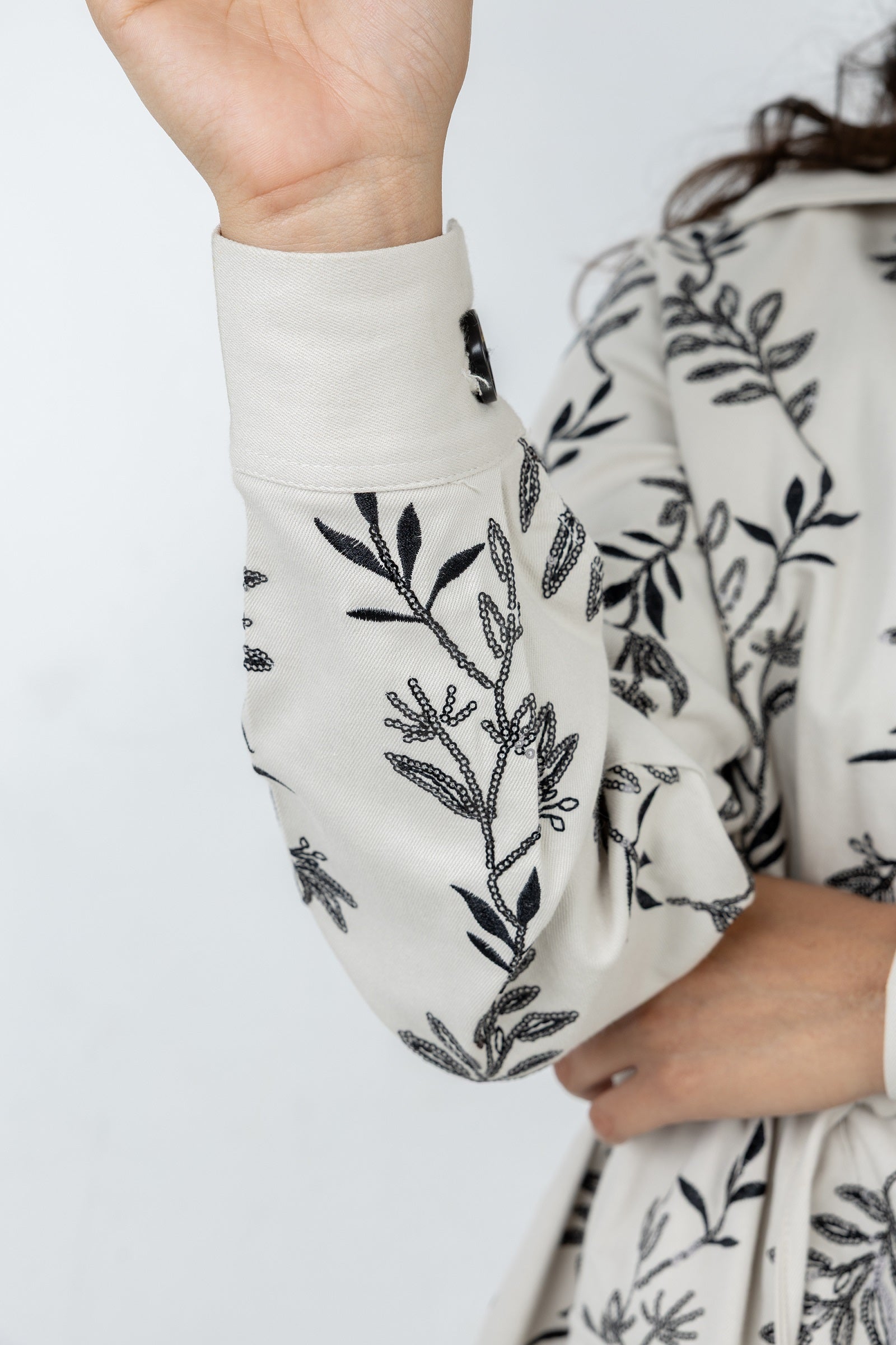 Person wearing a white garment with black floral patterns on a plain background