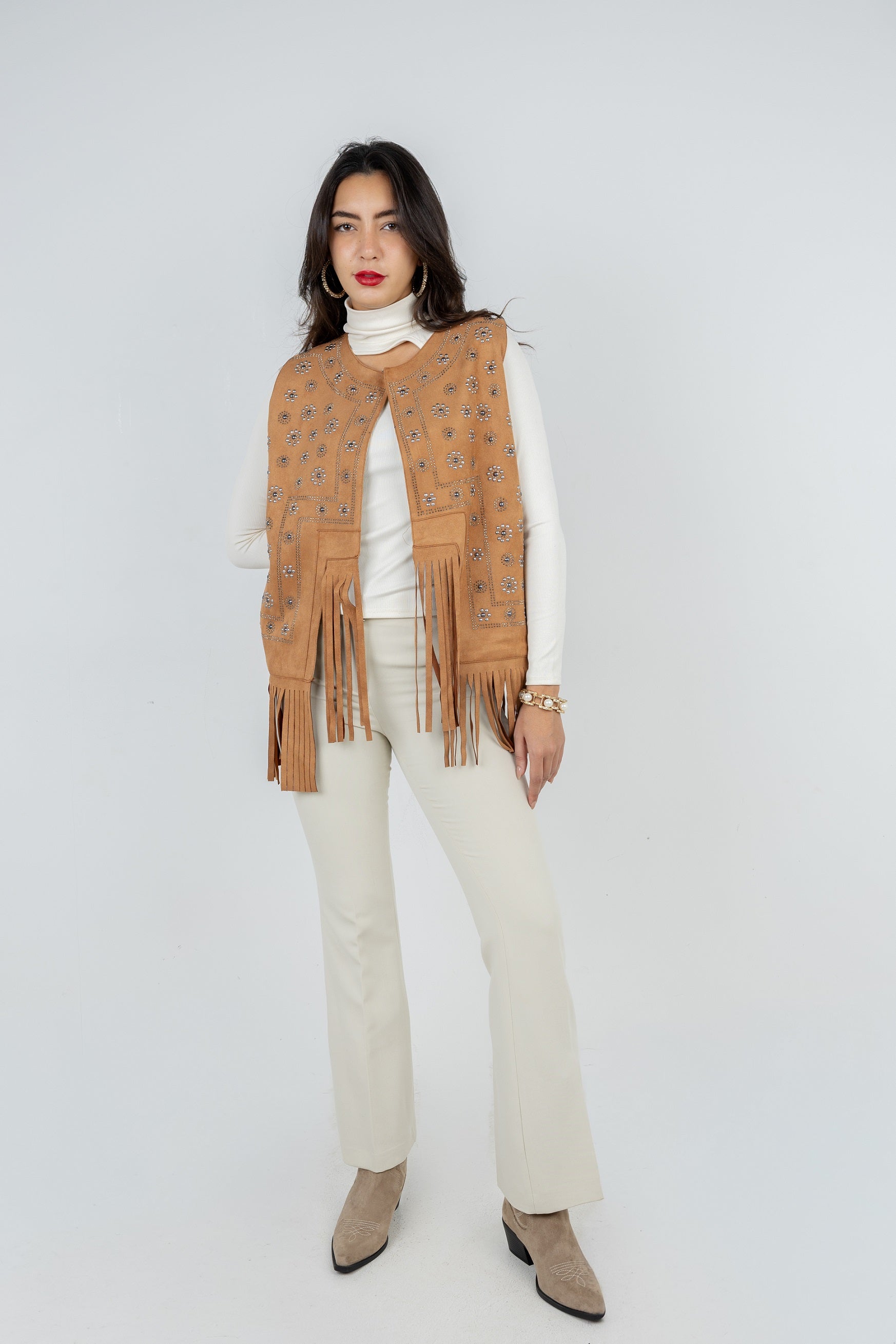 Woman wearing a brown fringed vest over a white top and beige pants on a white background