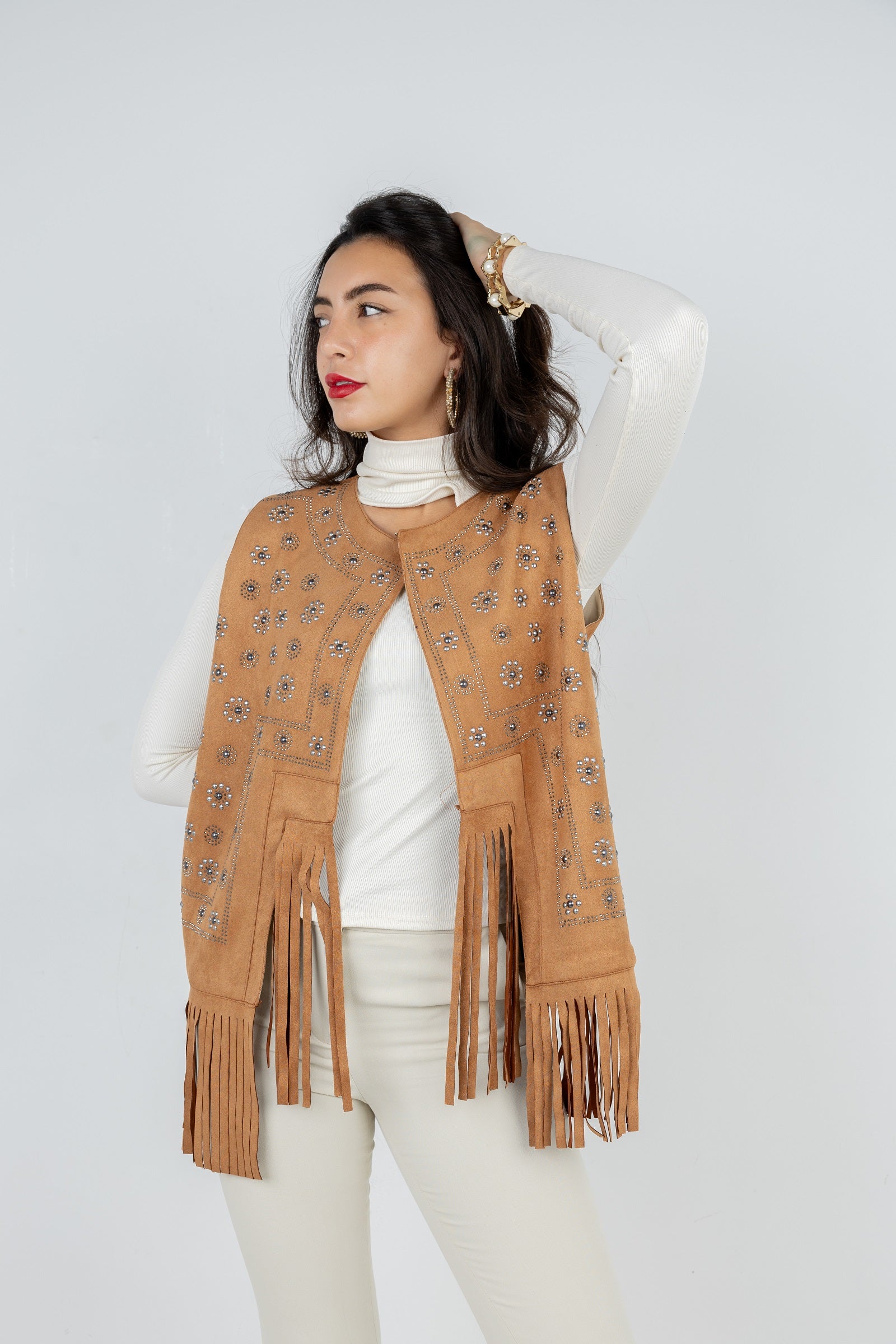 Woman wearing a tan fringe vest over a white top and pants on a white background