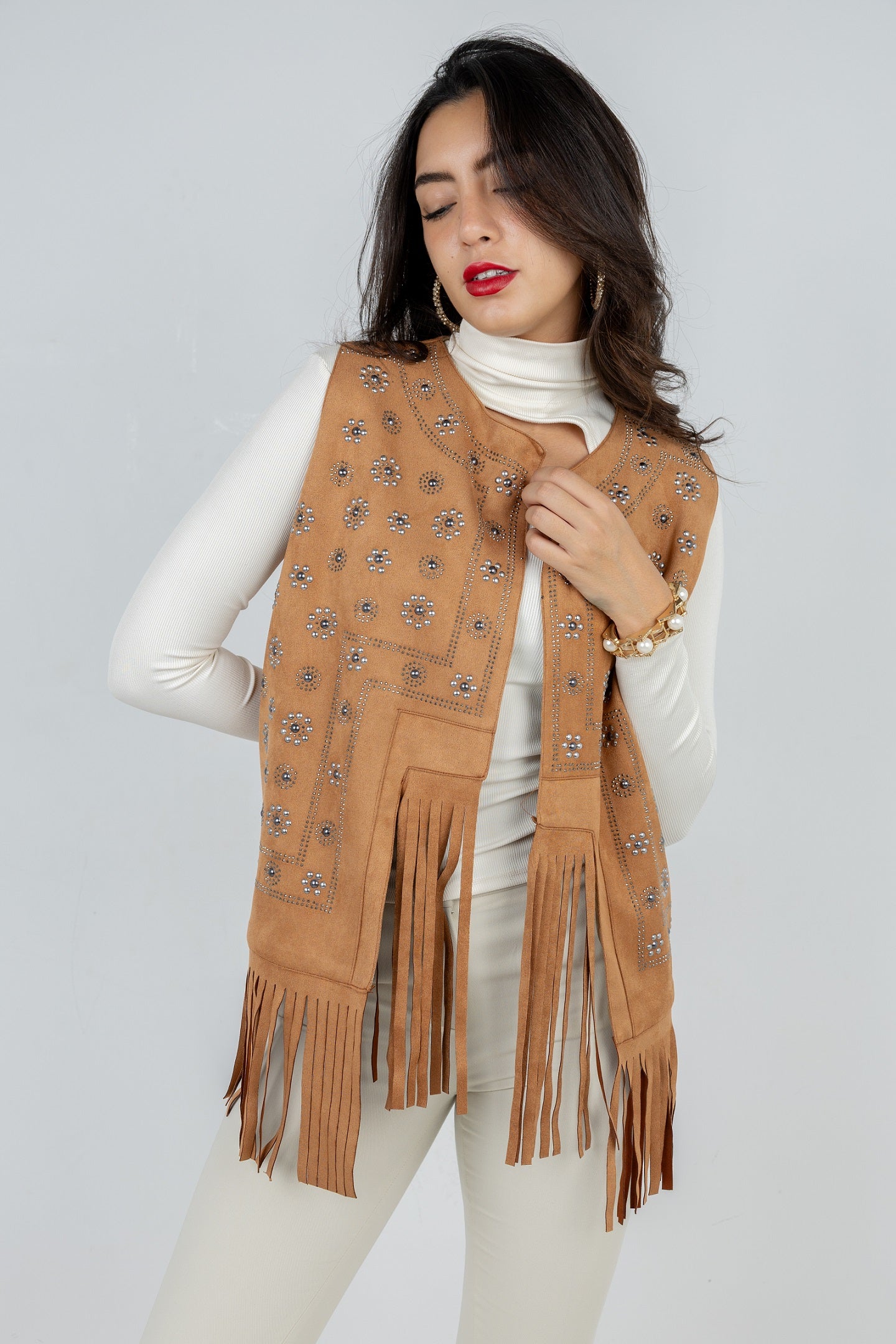 Woman wearing a tan fringe scarf with decorative patterns on a plain background