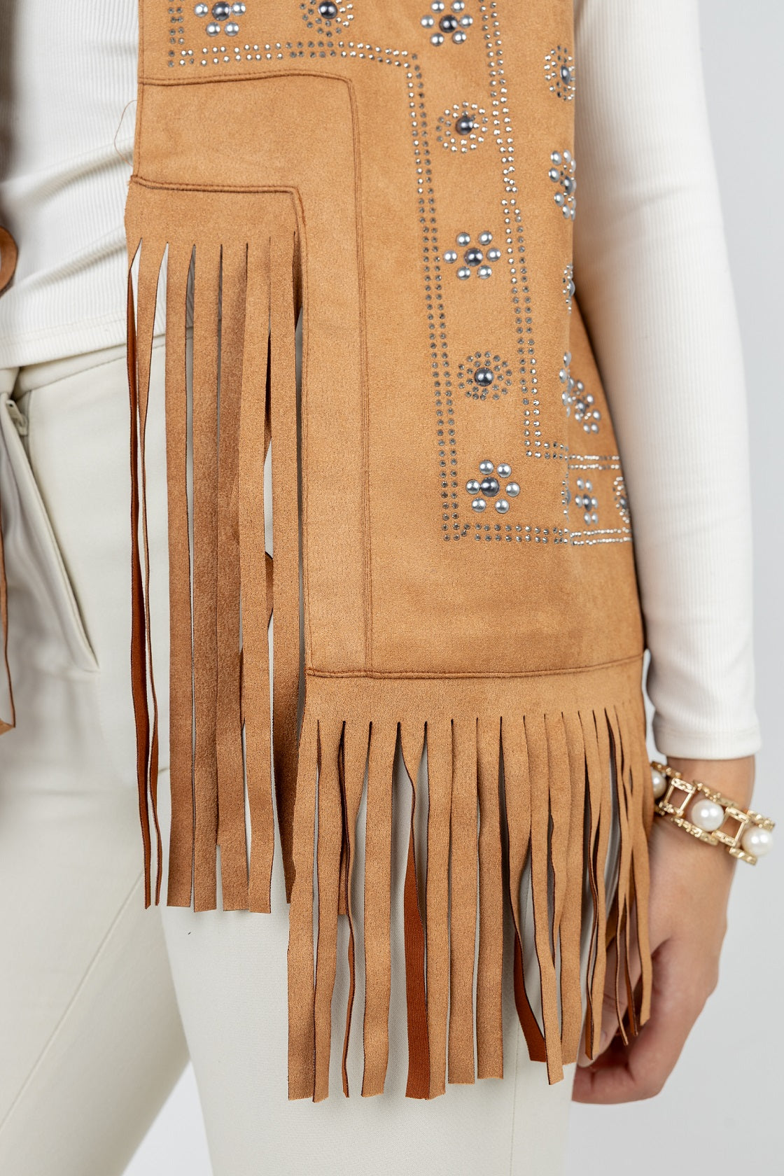 Tan suede vest with fringe and embellishments on a plain background