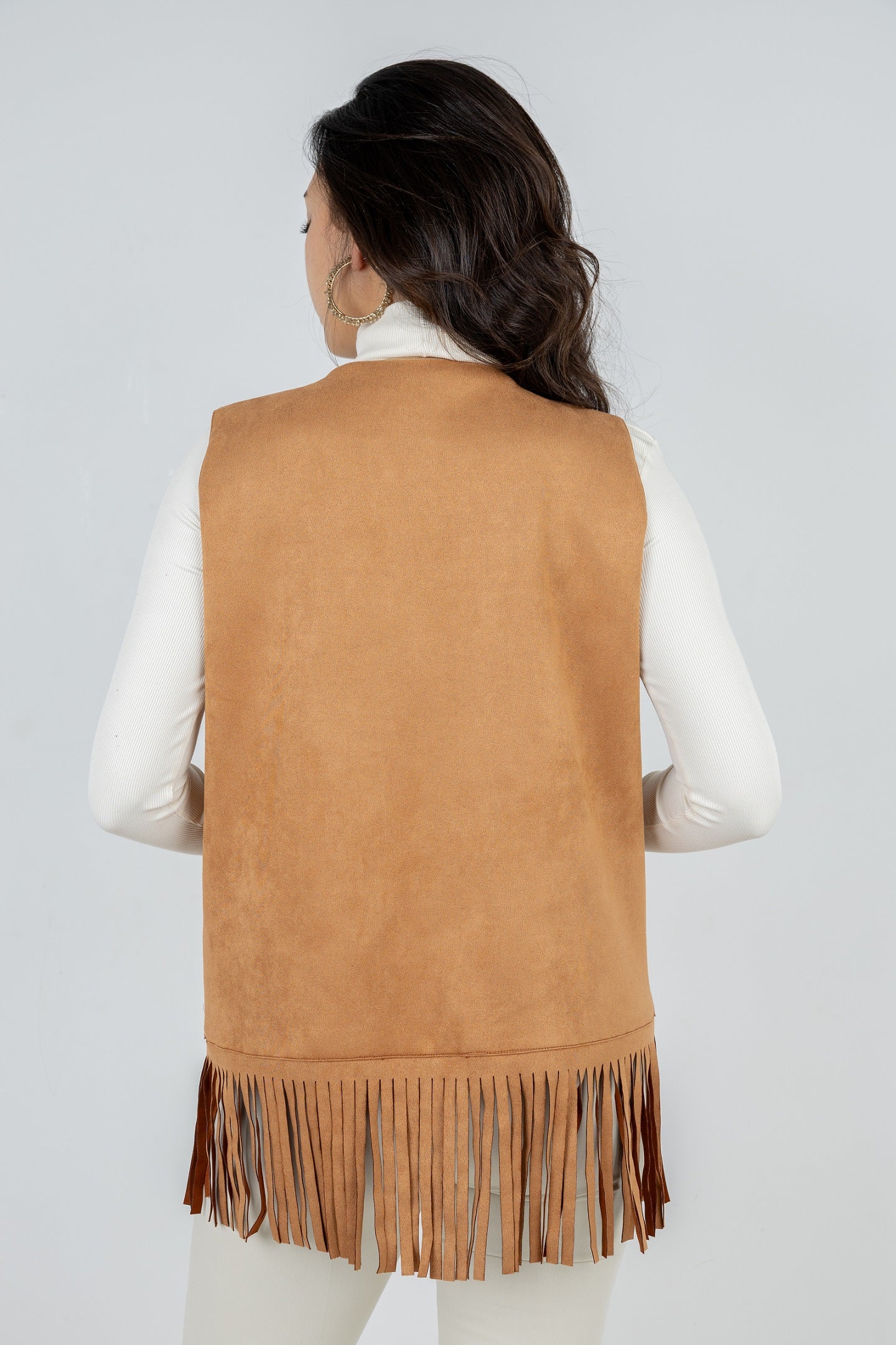 Person wearing a tan suede vest with fringe on a white background