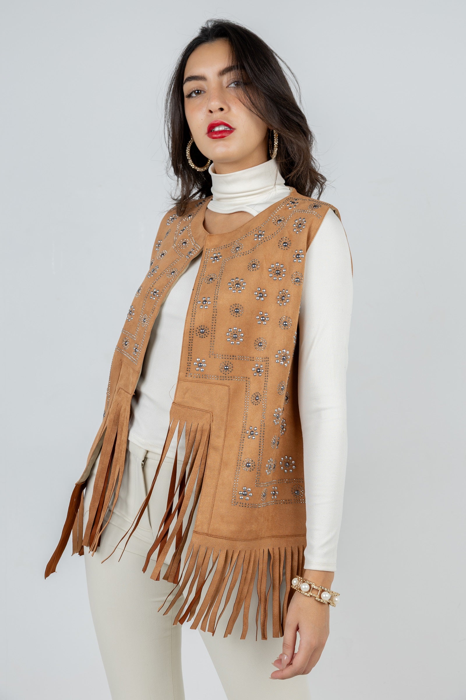 Woman wearing a brown suede vest with fringe details on a plain background