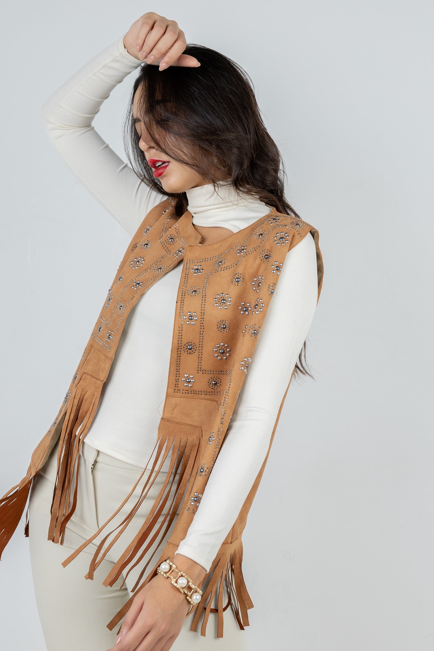 Woman wearing a brown fringe vest over a white top on a light gray background