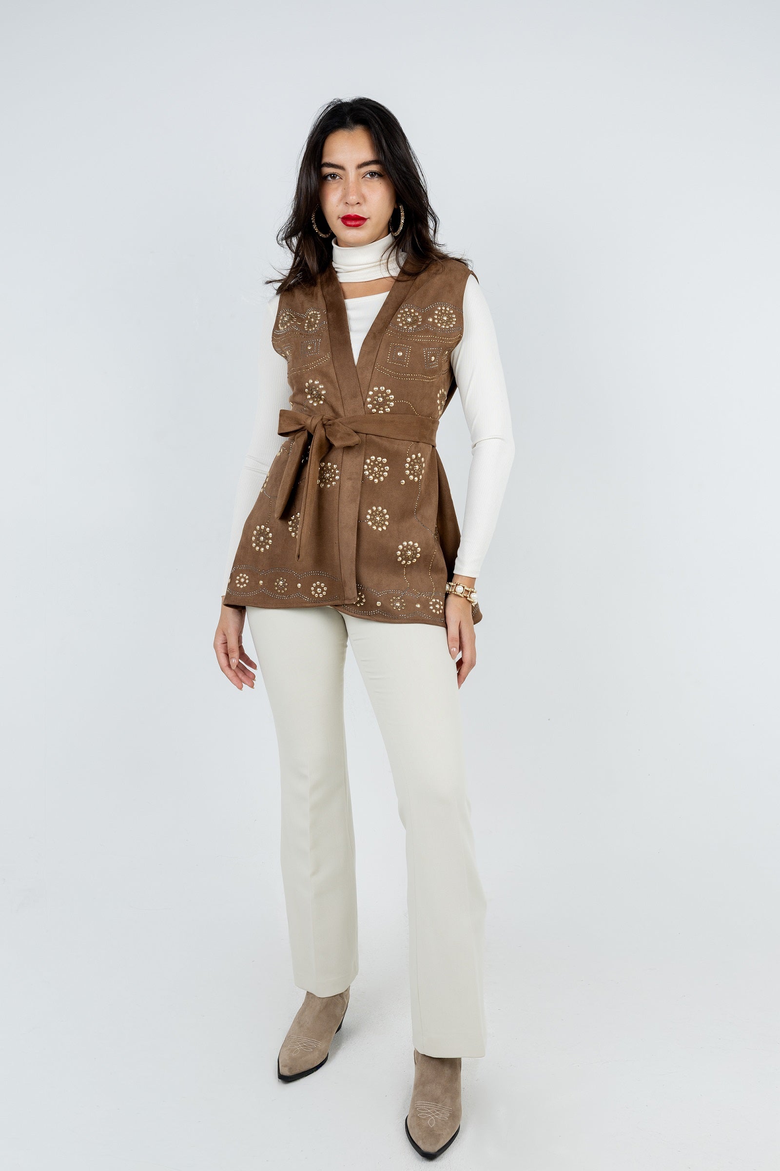 Woman wearing a brown patterned vest over a white shirt with beige pants on a white background