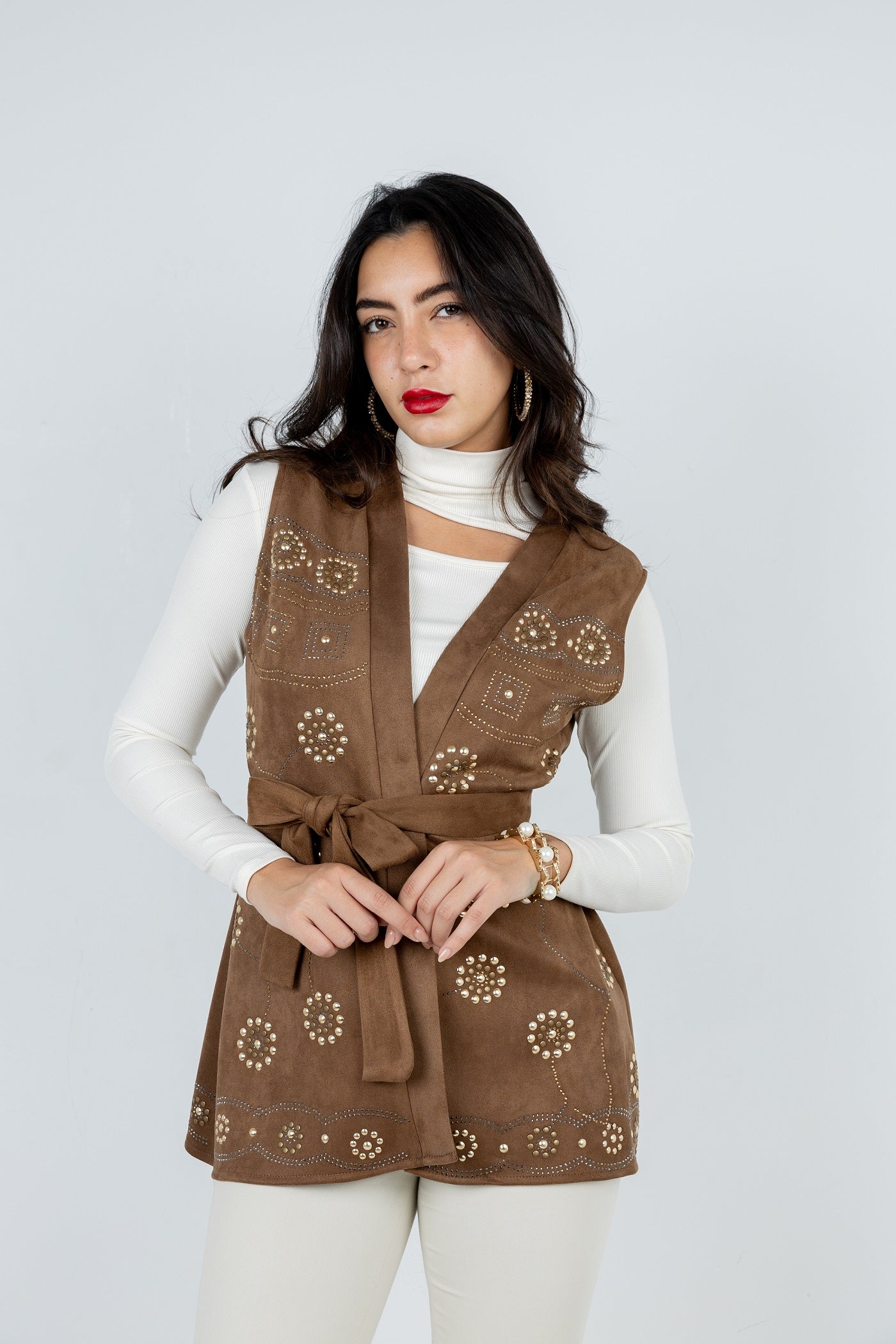 Woman wearing a brown embroidered vest over a white top against a light gray background