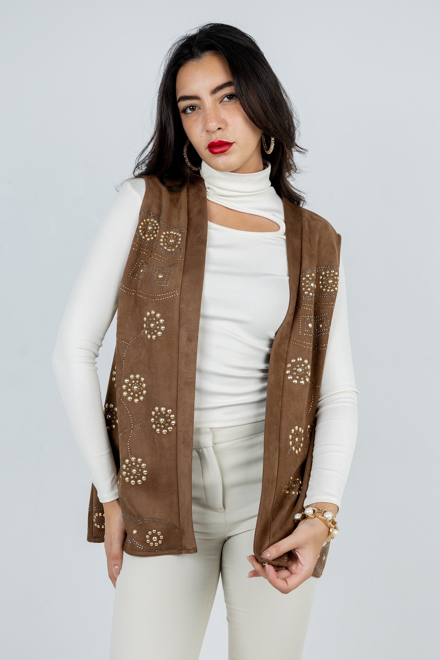 Woman wearing a brown embroidered vest over a white outfit on a light gray background