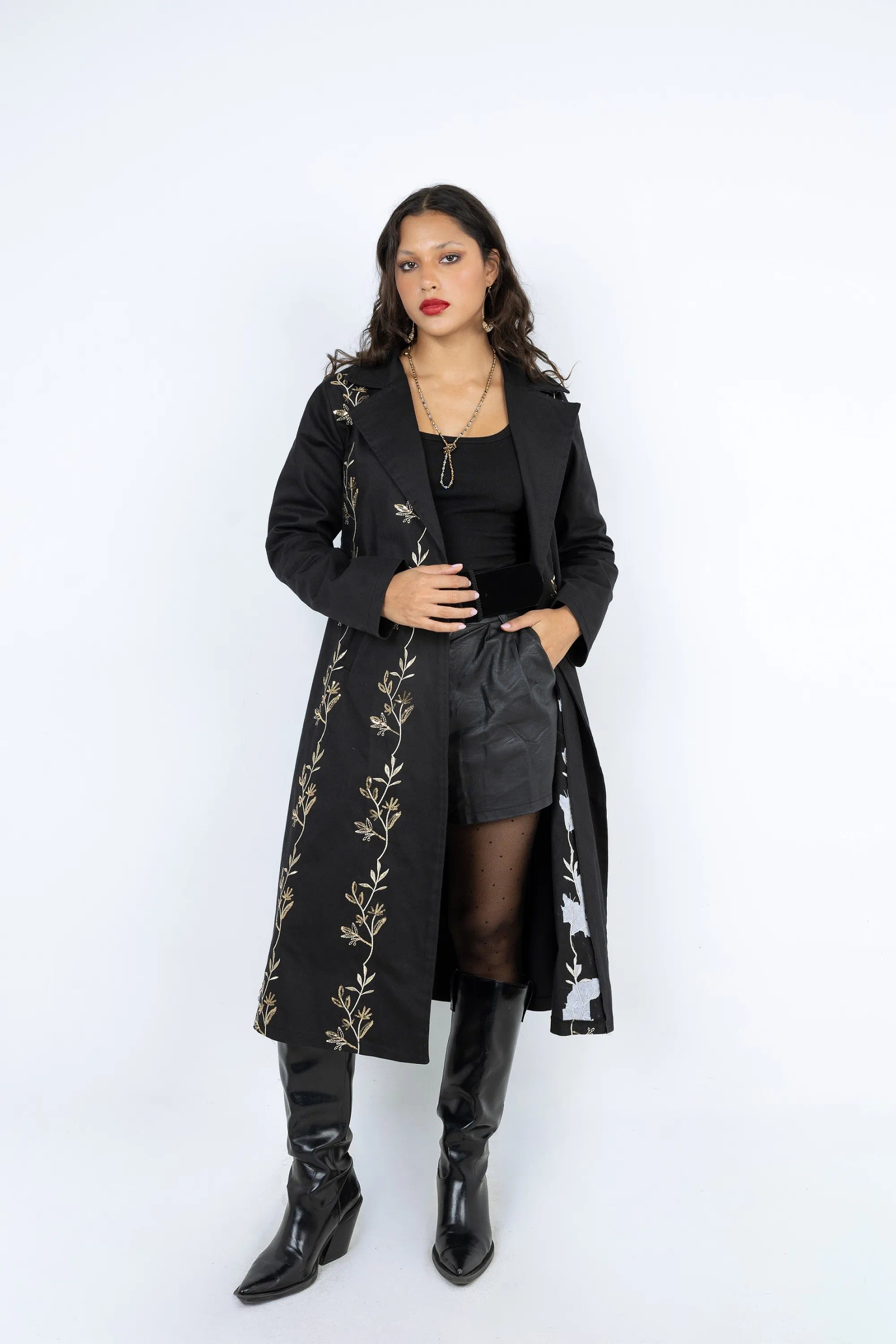 Woman wearing a black coat with floral embroidery, black top, and black boots on a white background