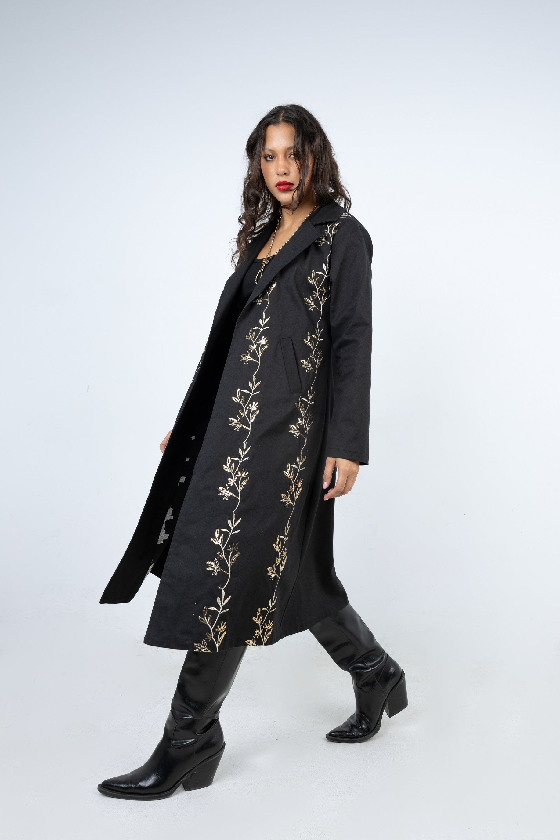 Woman wearing a long black coat with gold embroidery on a white background