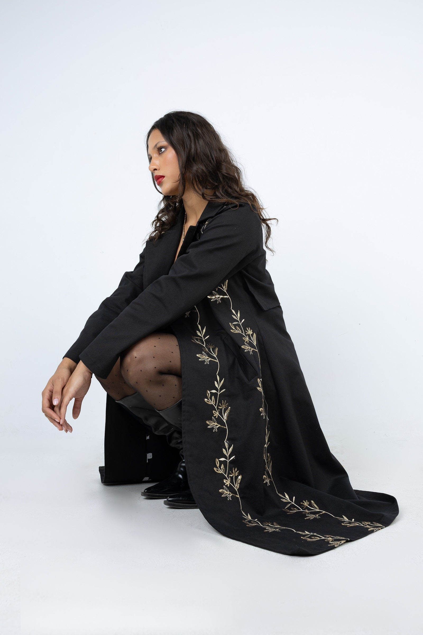Woman wearing a black dress with gold embroidery on a white background