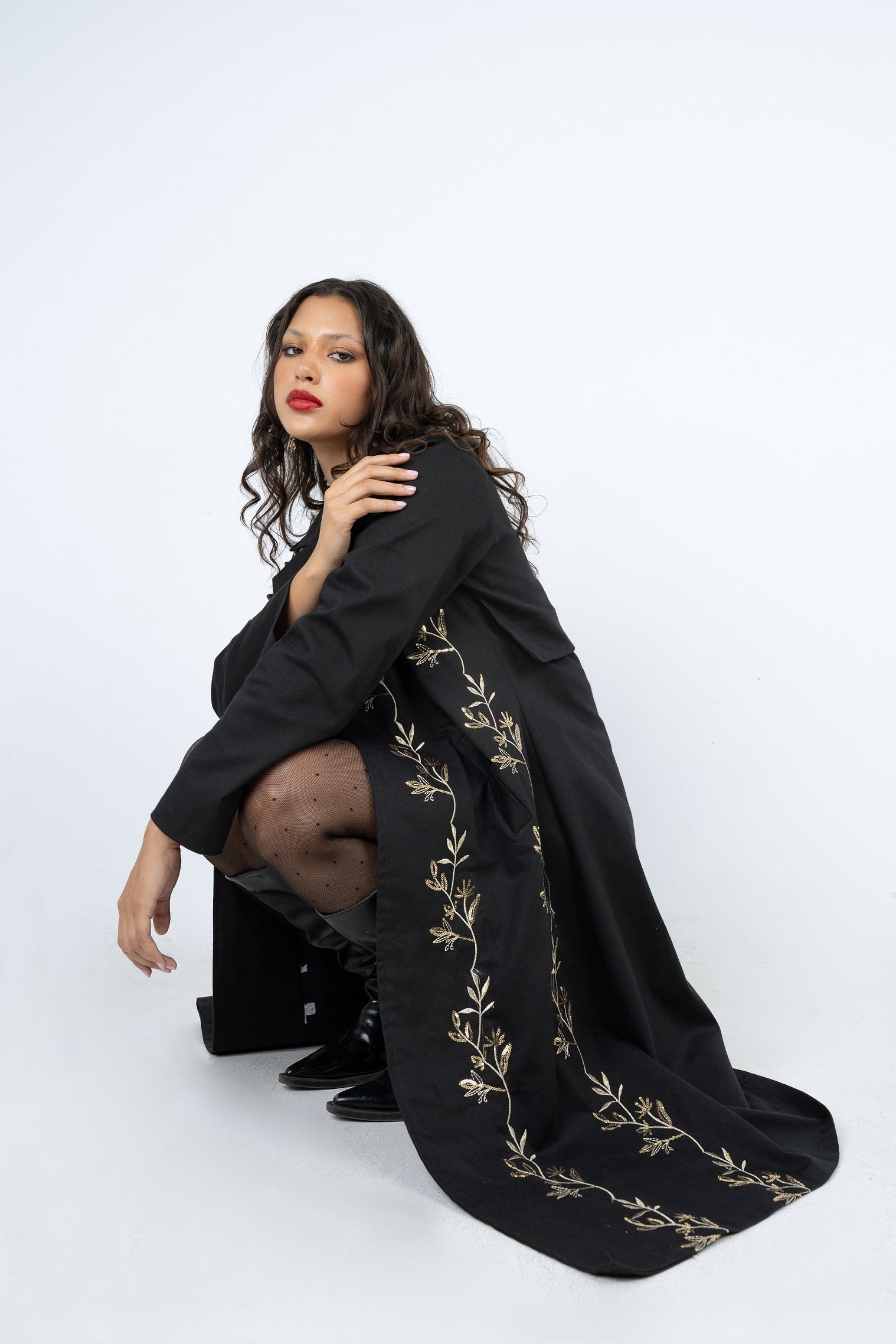 Woman wearing a black dress with gold embroidery on a white background