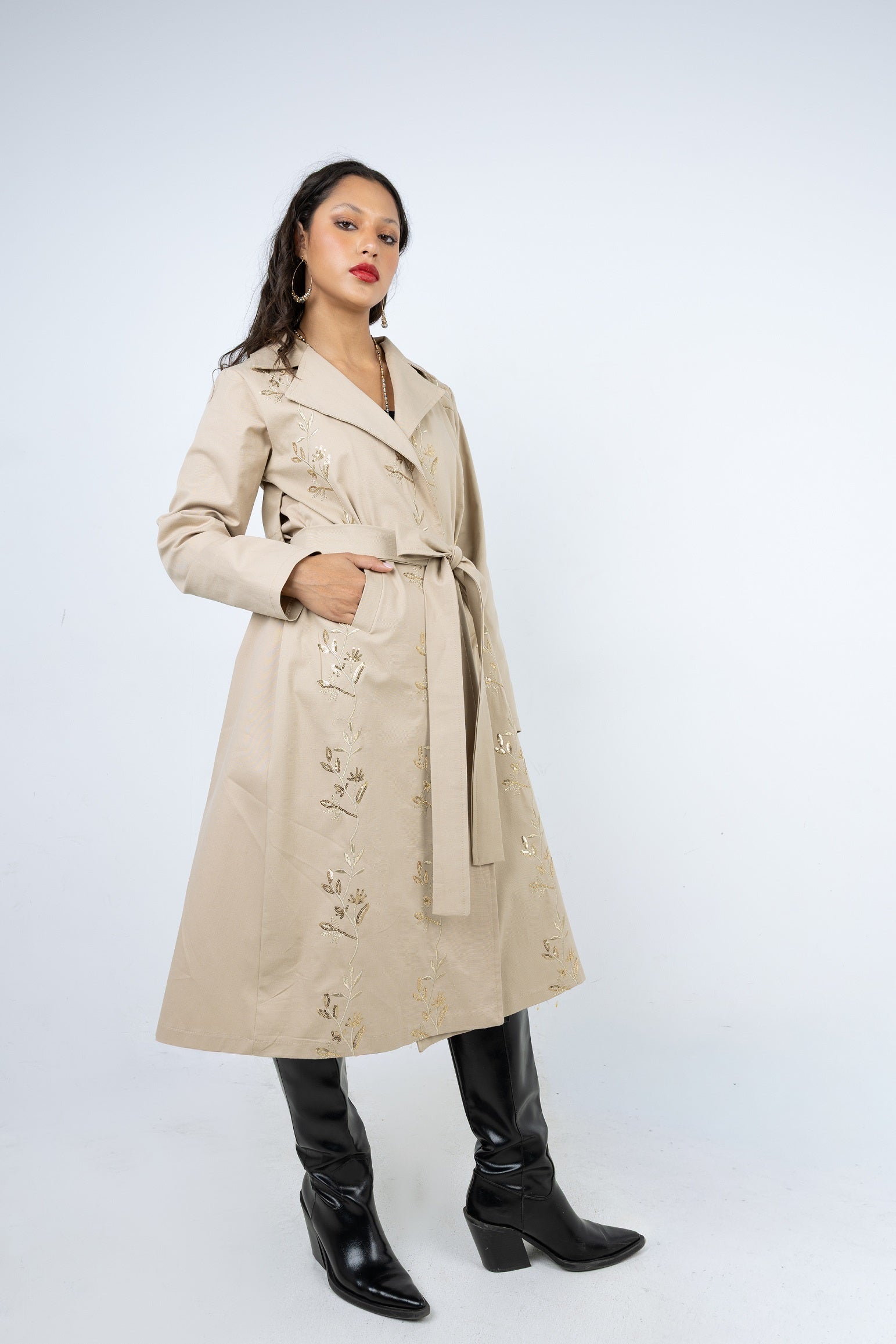 Woman wearing a beige trench coat with floral embroidery on a white background