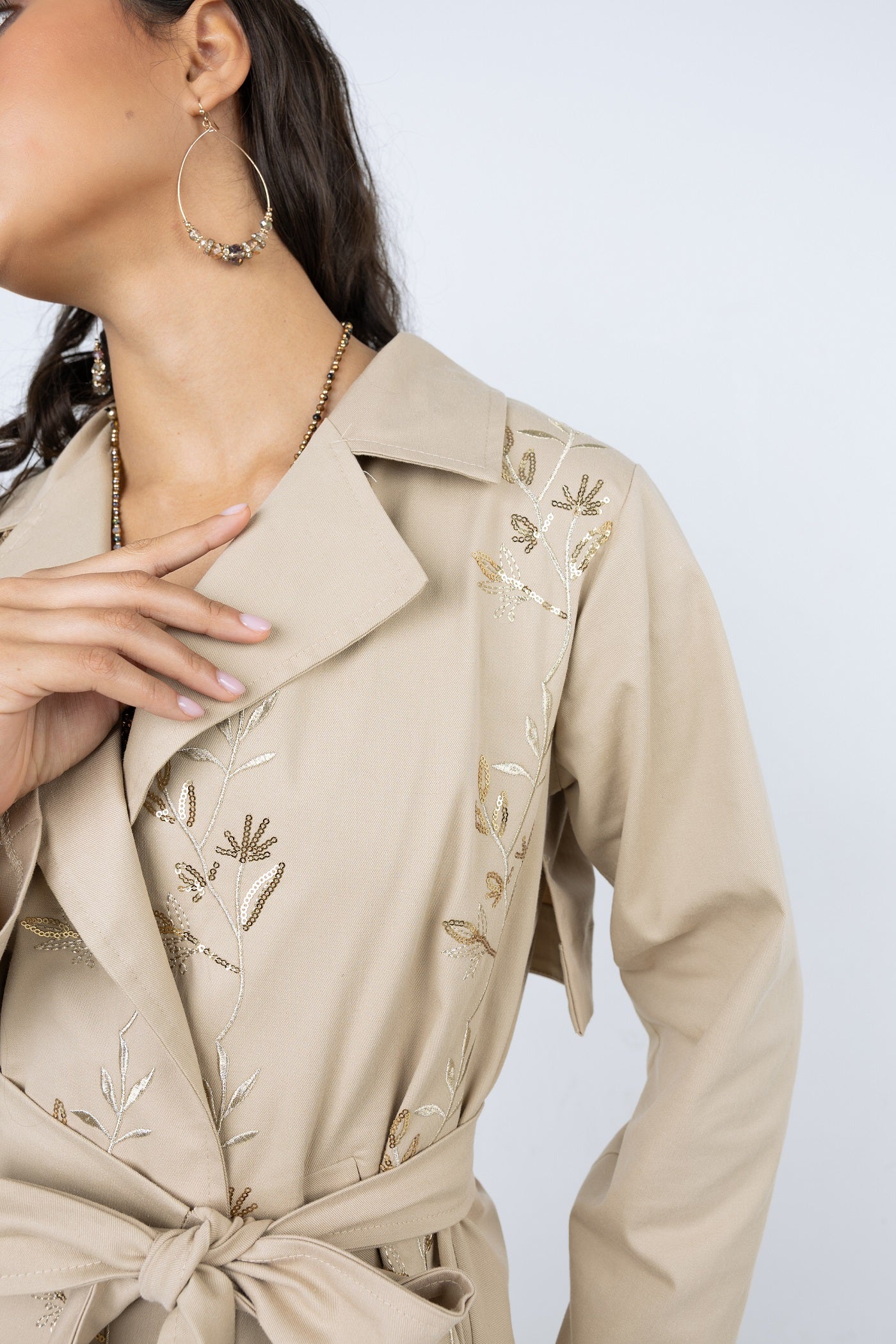 Beige trench coat with floral embroidery on a plain background