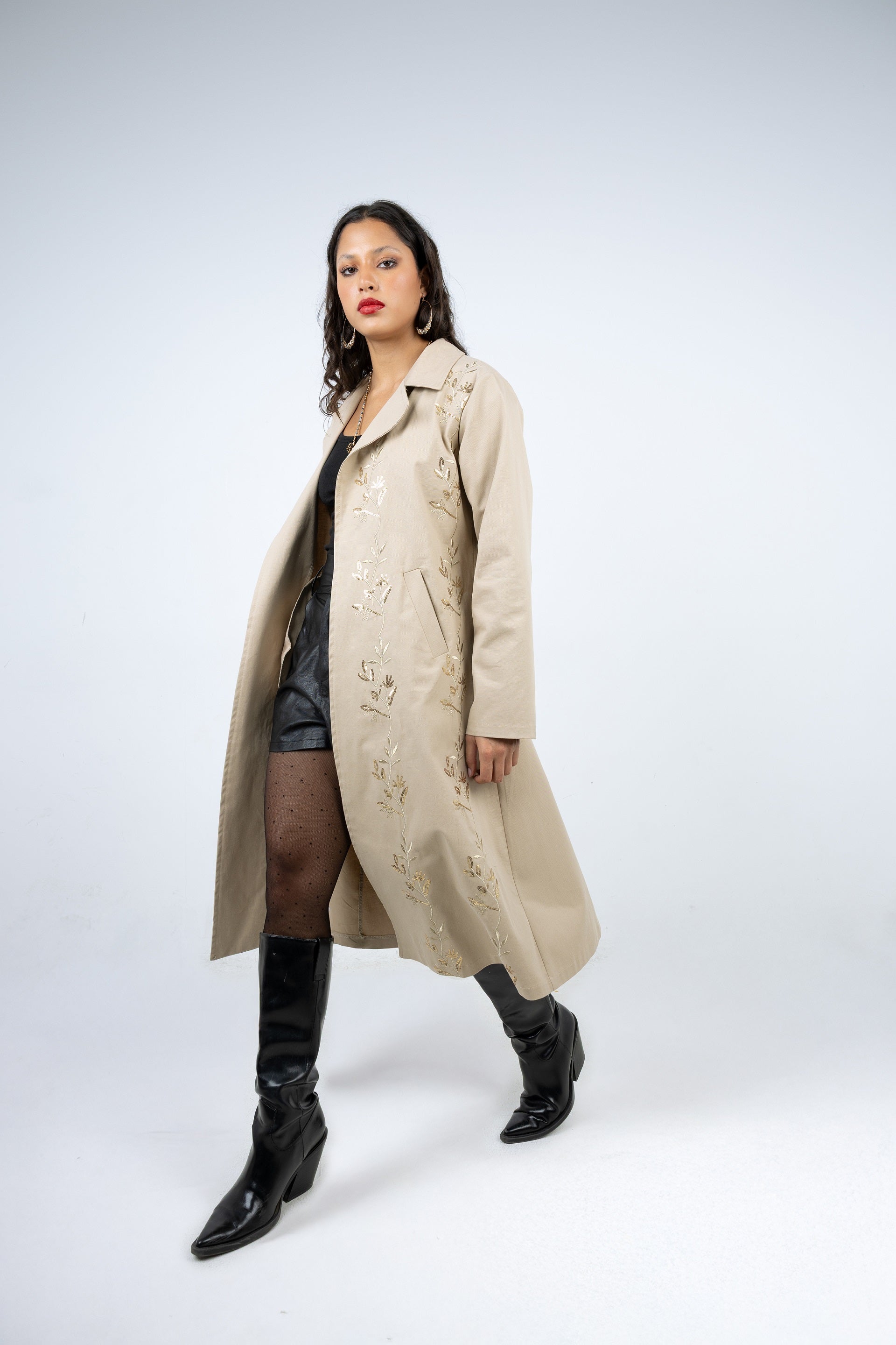 Woman wearing a beige trench coat and black knee-high boots on a white background