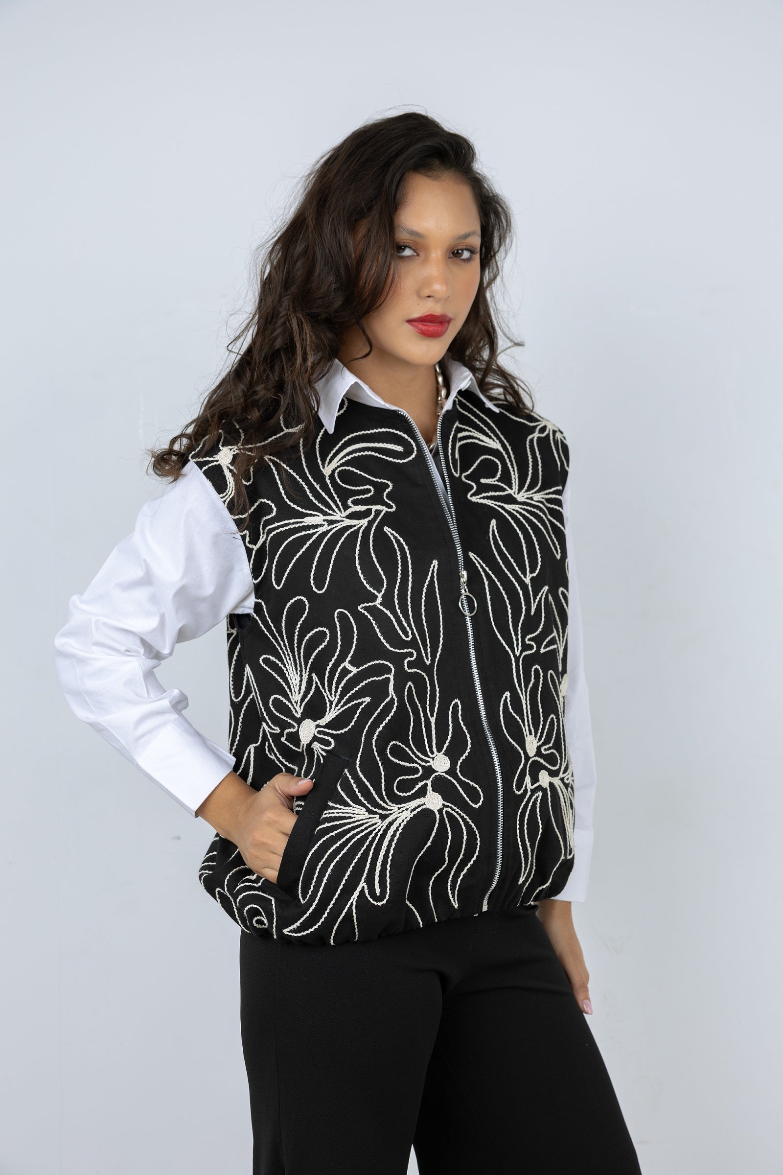 Woman wearing a black floral patterned shirt over a white blouse with a plain background