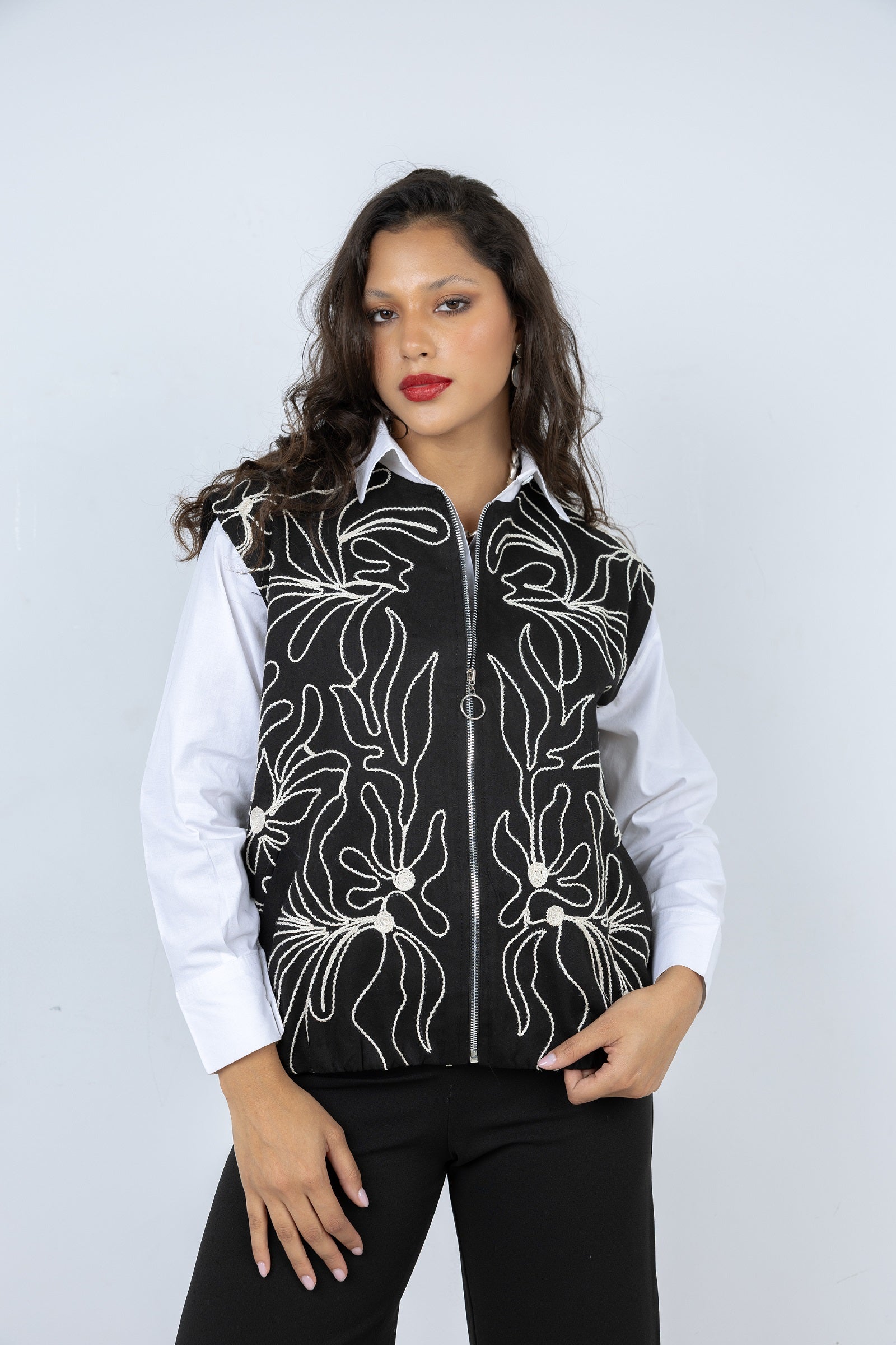 Woman wearing a black vest with white floral patterns on a plain background