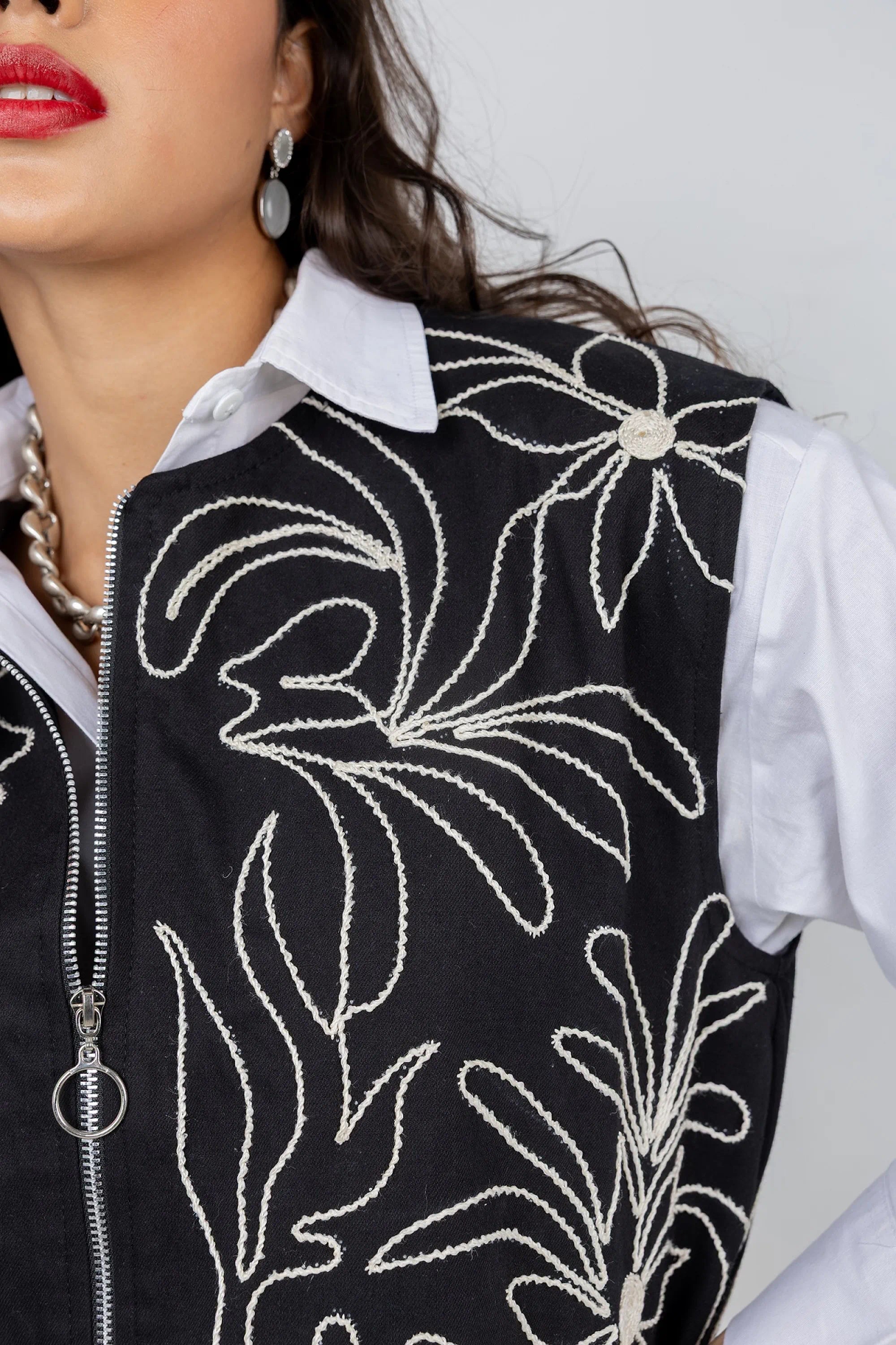 Person wearing a black vest with white floral embroidery on a plain background