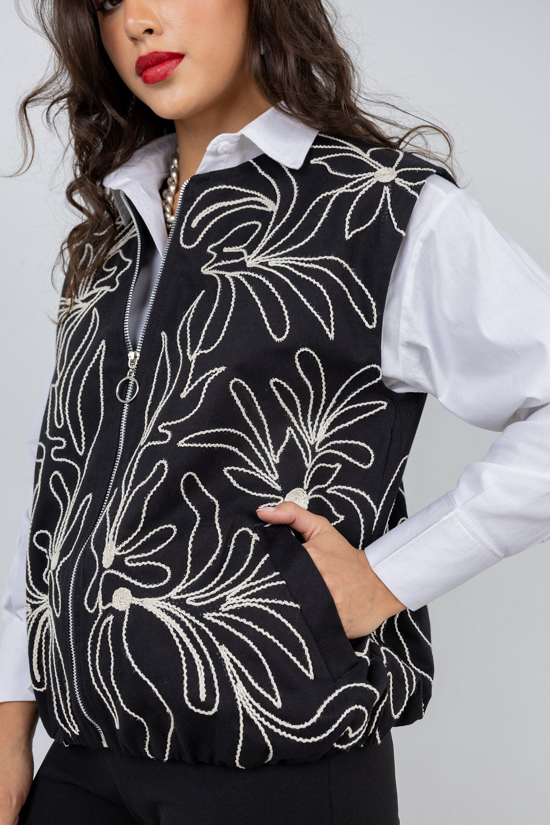 Woman wearing a black vest with white floral patterns on a plain background