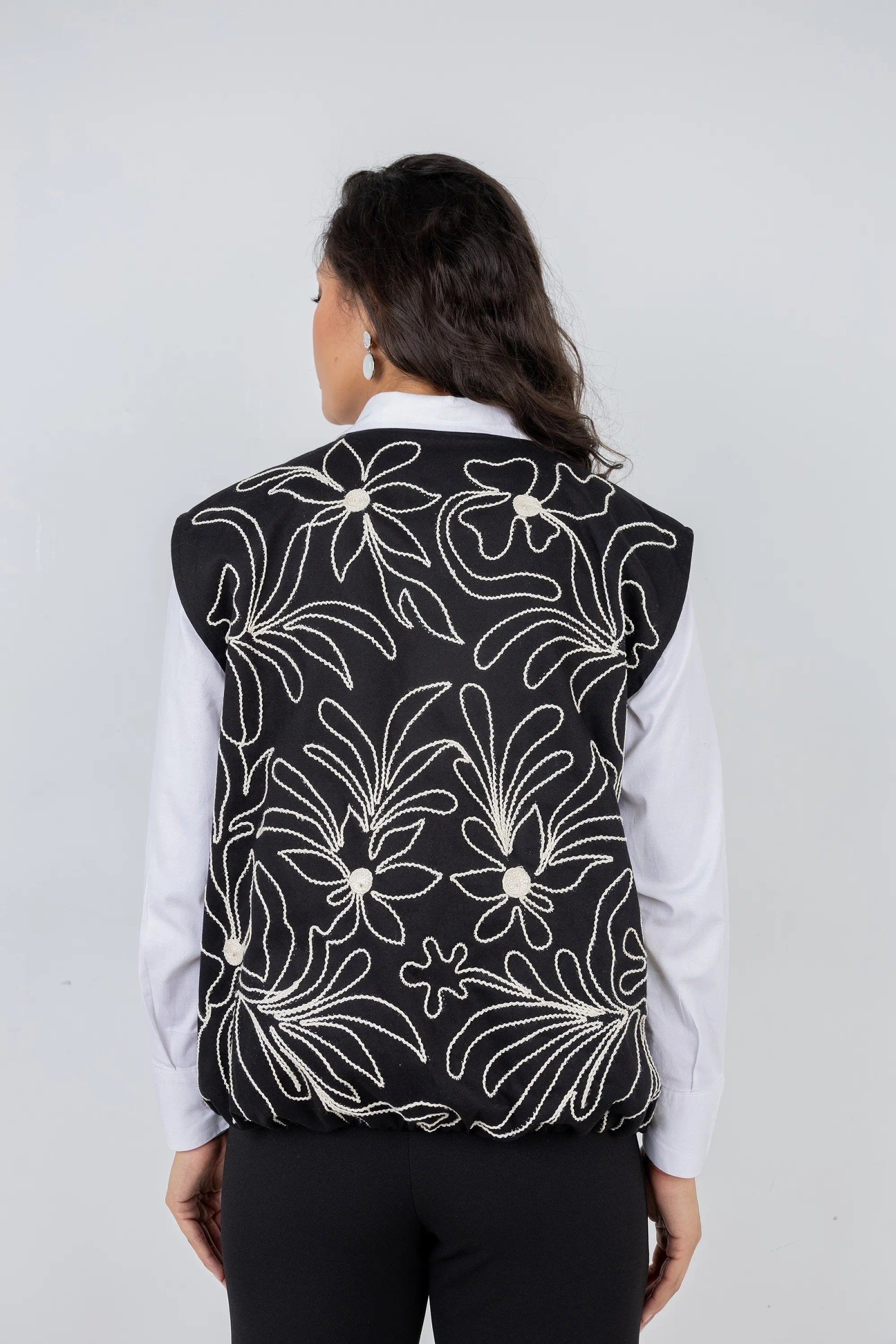 Person wearing a black floral-patterned vest over a white shirt on a gray background